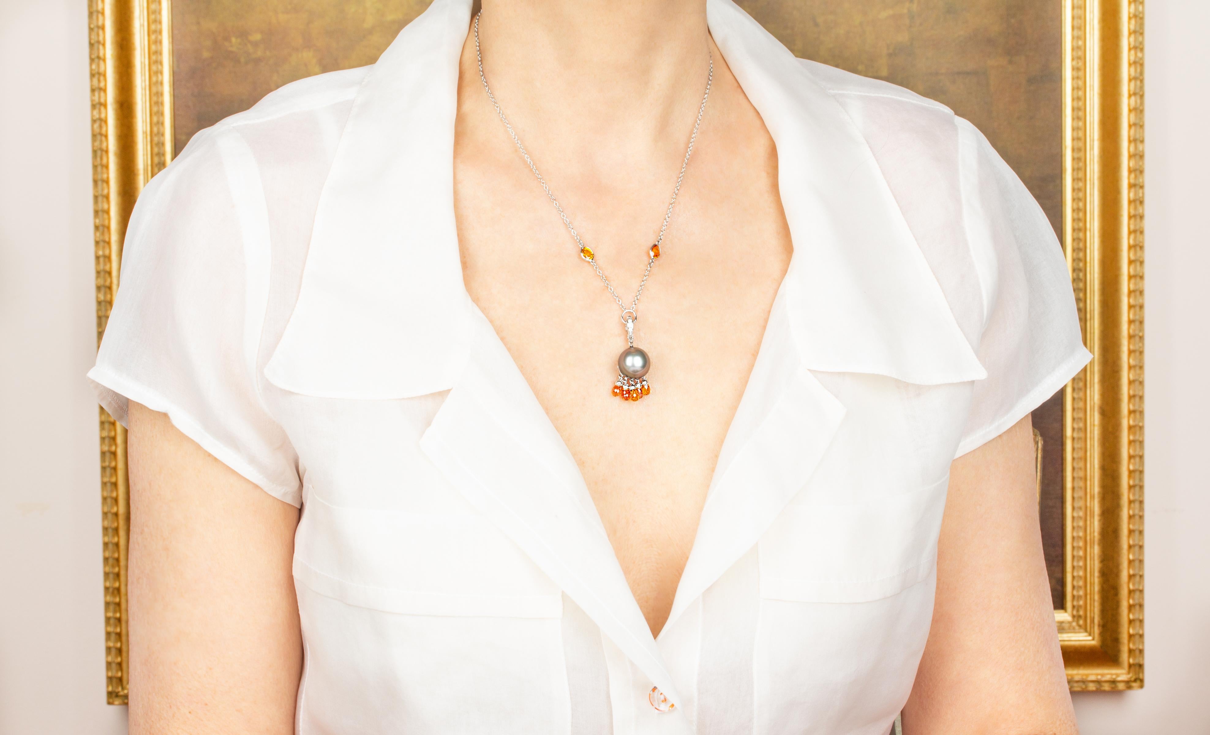 This pearl pendant necklace features a Tahitian pearl of 13.5mm diameter suspending 5 orange briolette sapphires. It hangs by a hook set with diamonds to a 17” 18 carat white gold chain decorated with 2 motifs of orange sapphire. The pendant is