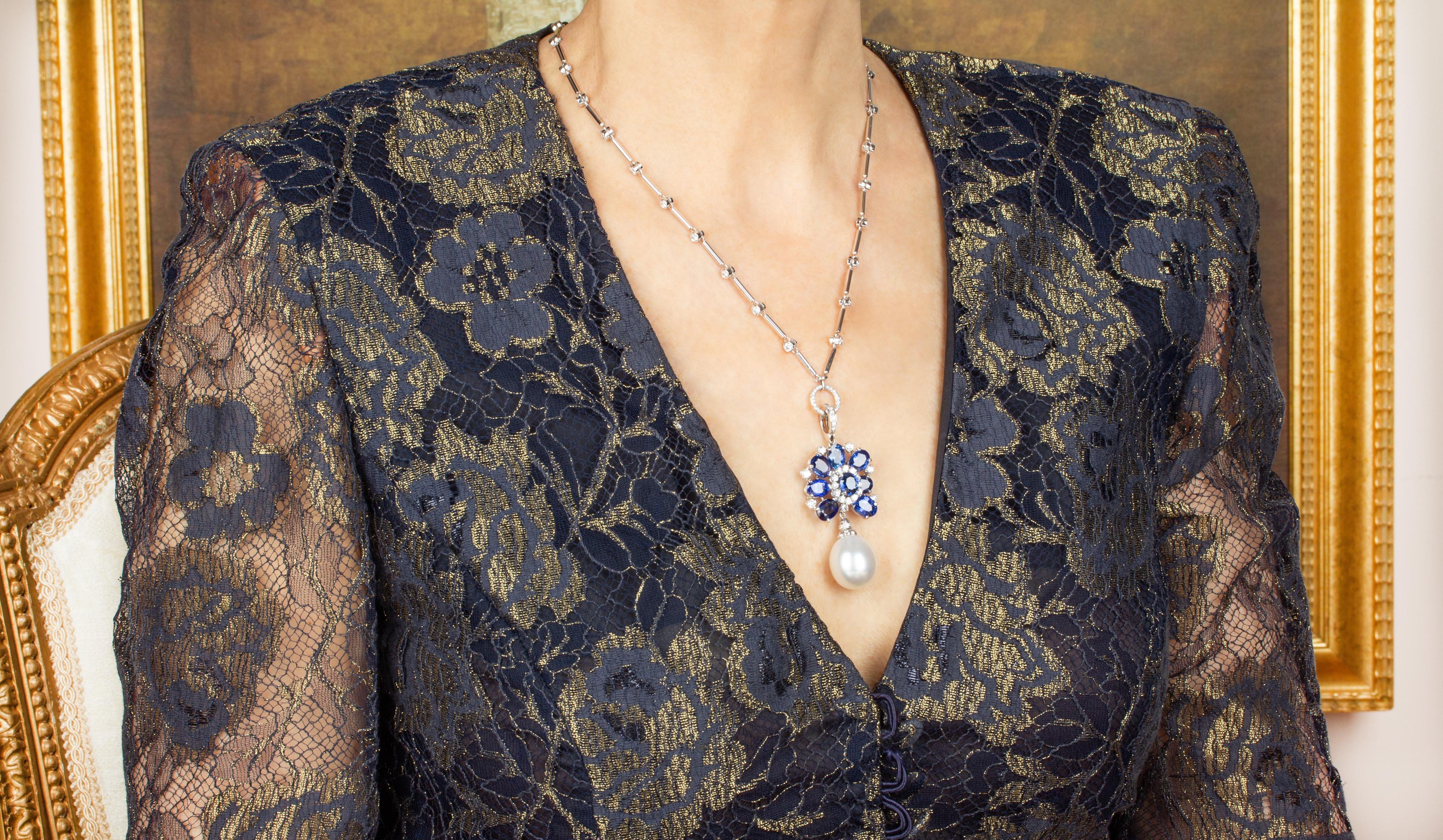 The blue sapphire and diamond pendant features an arrangement of oval shape faceted sapphires accented with a crown of round diamonds. The jewel suspends a splendid South Sea pearl of the unusual size of 18mm. The 2.25” pendant is accompanied by an