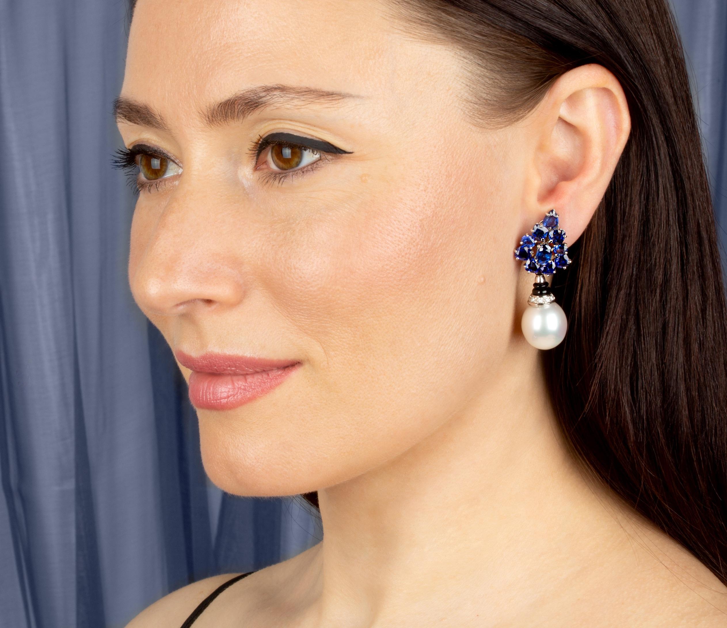 The blue sapphire and South Sea pearl earrings feature a spray of 13.50 carats of oval cut and pear shape faceted Ceylon sapphires. The tops suspend- via an onyx ring- 2 South Sea pearls of 15 x 16mm. The design is complete with 0.20 carats of round