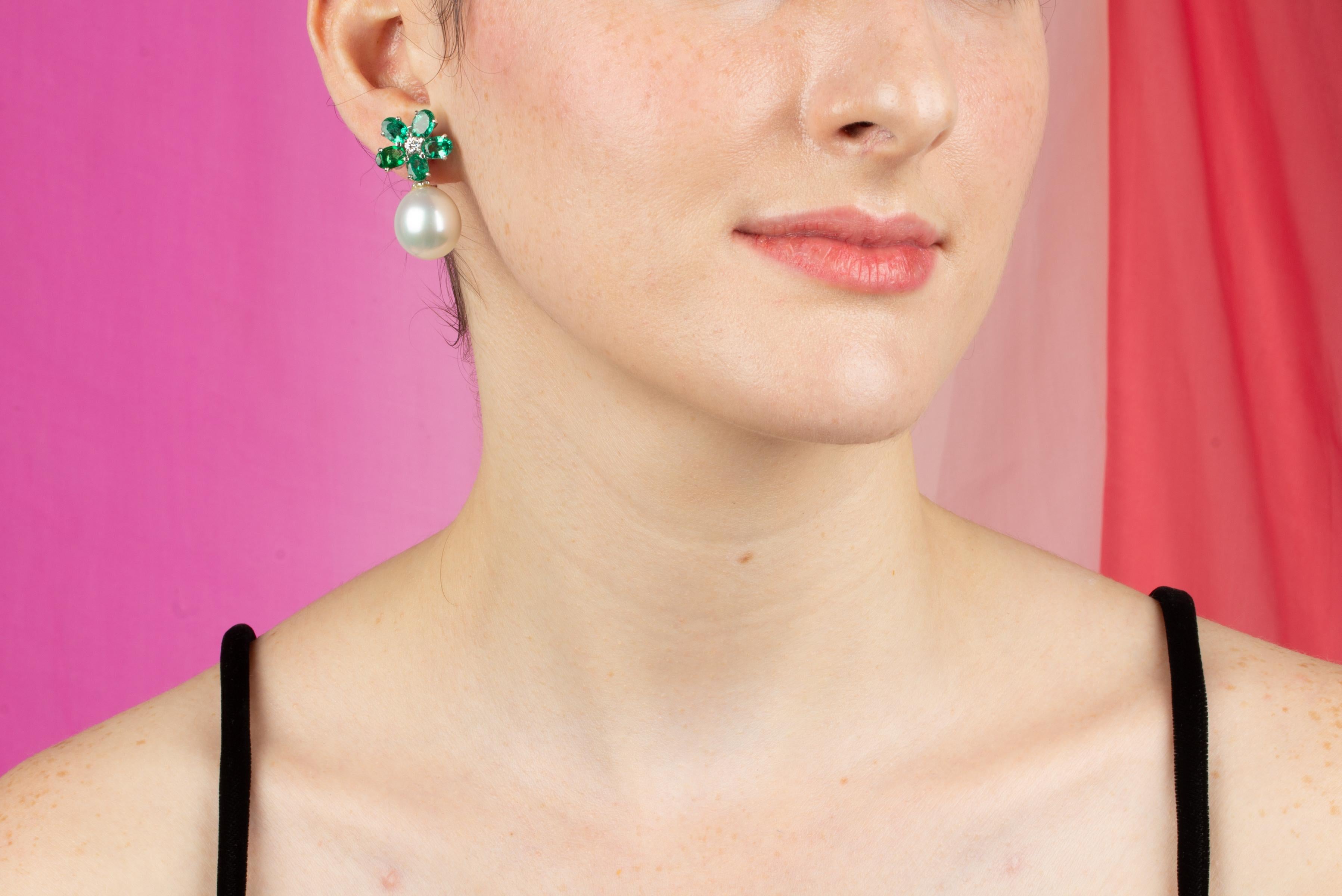The emerald and South Sea pearl earrings feature a flower design on the ear with 4.80 carats of oval shape faceted Zambian emeralds of brilliant crystalline color and texture. The tops suspend 2 South Sea pearls of 17 x 15mm diameter. 0.36 carats of