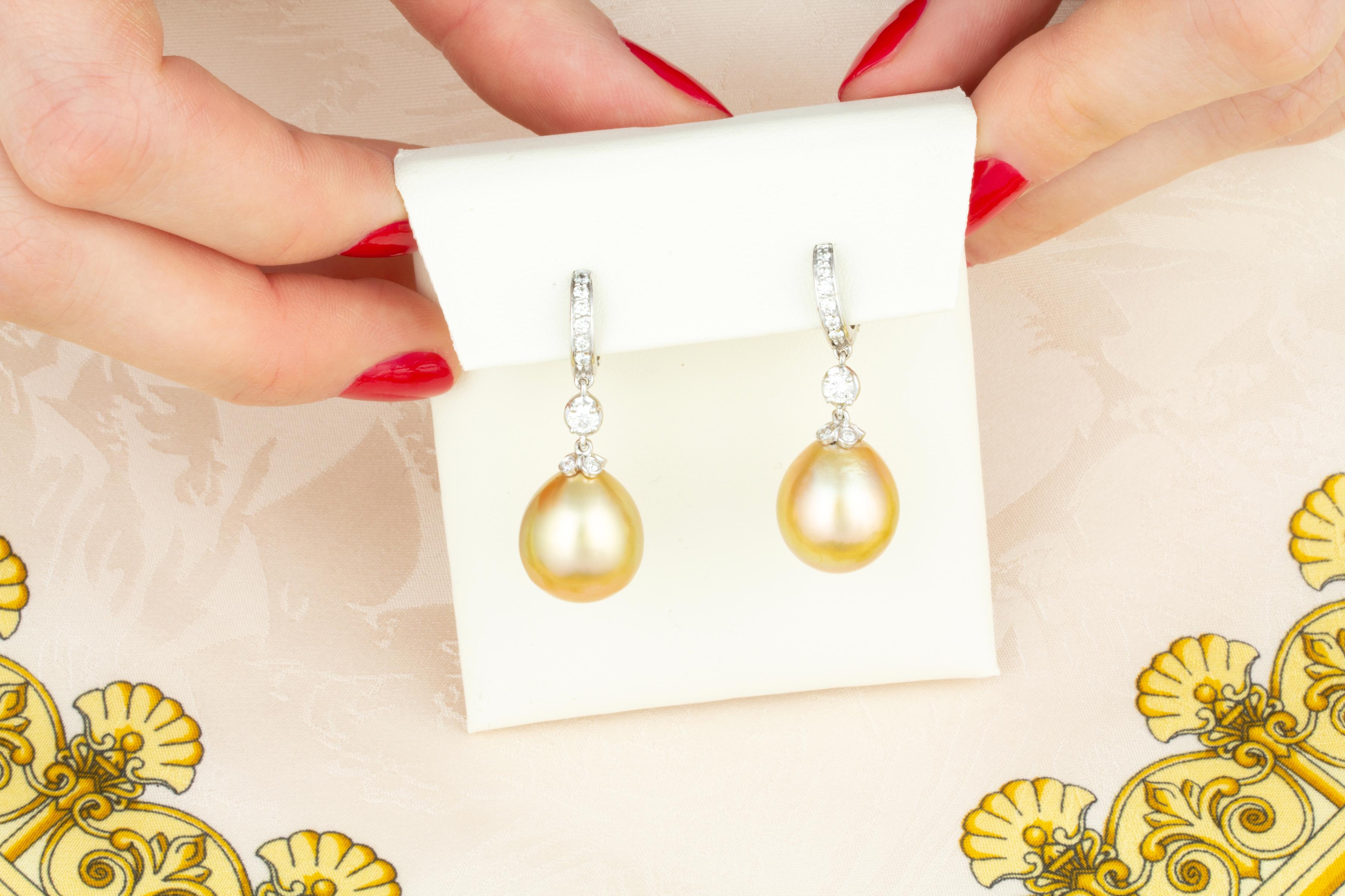 Les boucles d'oreilles pendantes en perles dorées et diamants sont composées de deux perles de 15 x 13 mm de nacre de qualité, d'un bel éclat et d'une couleur dorée intense.
Les perles sont suspendues à des anneaux sertis de diamants ronds en pavé