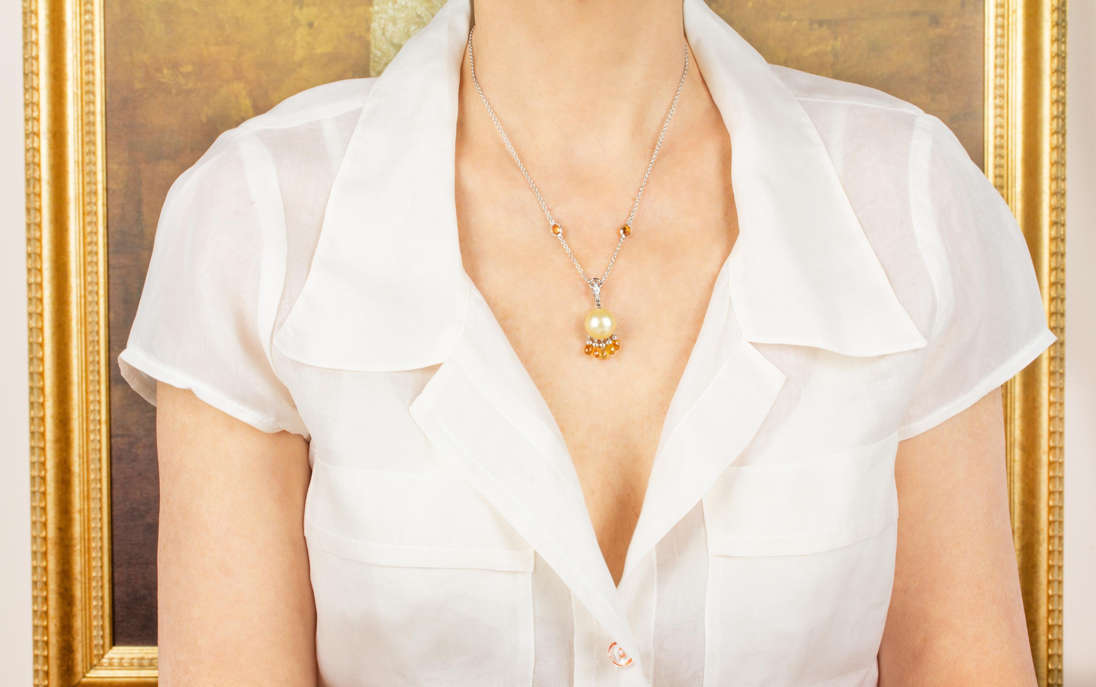 This pearl, sapphire and diamond pendant necklace features a golden South Sea pearl of 14mm diameter suspending 5 orange briolette sapphires of fiery color. The pendant hangs from a hook set with diamonds and connects to a 16.5” 18 carat white gold