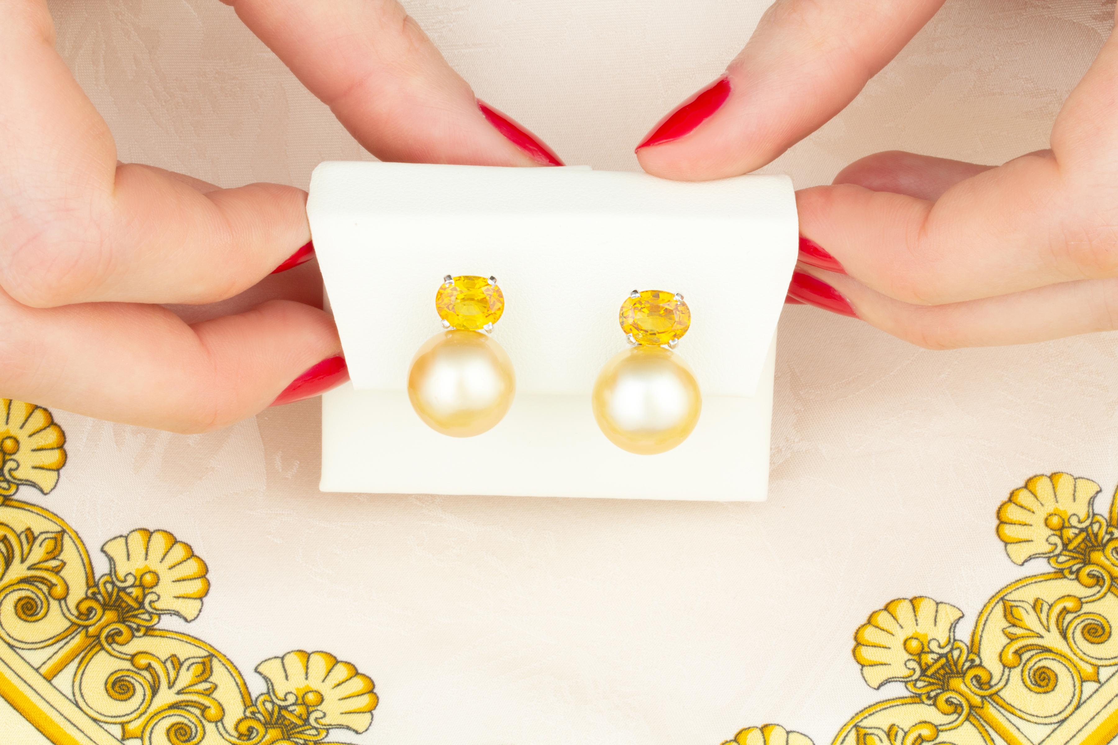 The sapphire and pearl earrings feature two 13.5mm South Sea pearls from the waters of Northwestern Australia. The pearls display beautiful nacre and a lovely golden color. They are untreated. The design is complete with 2 faceted oval cut yellow
