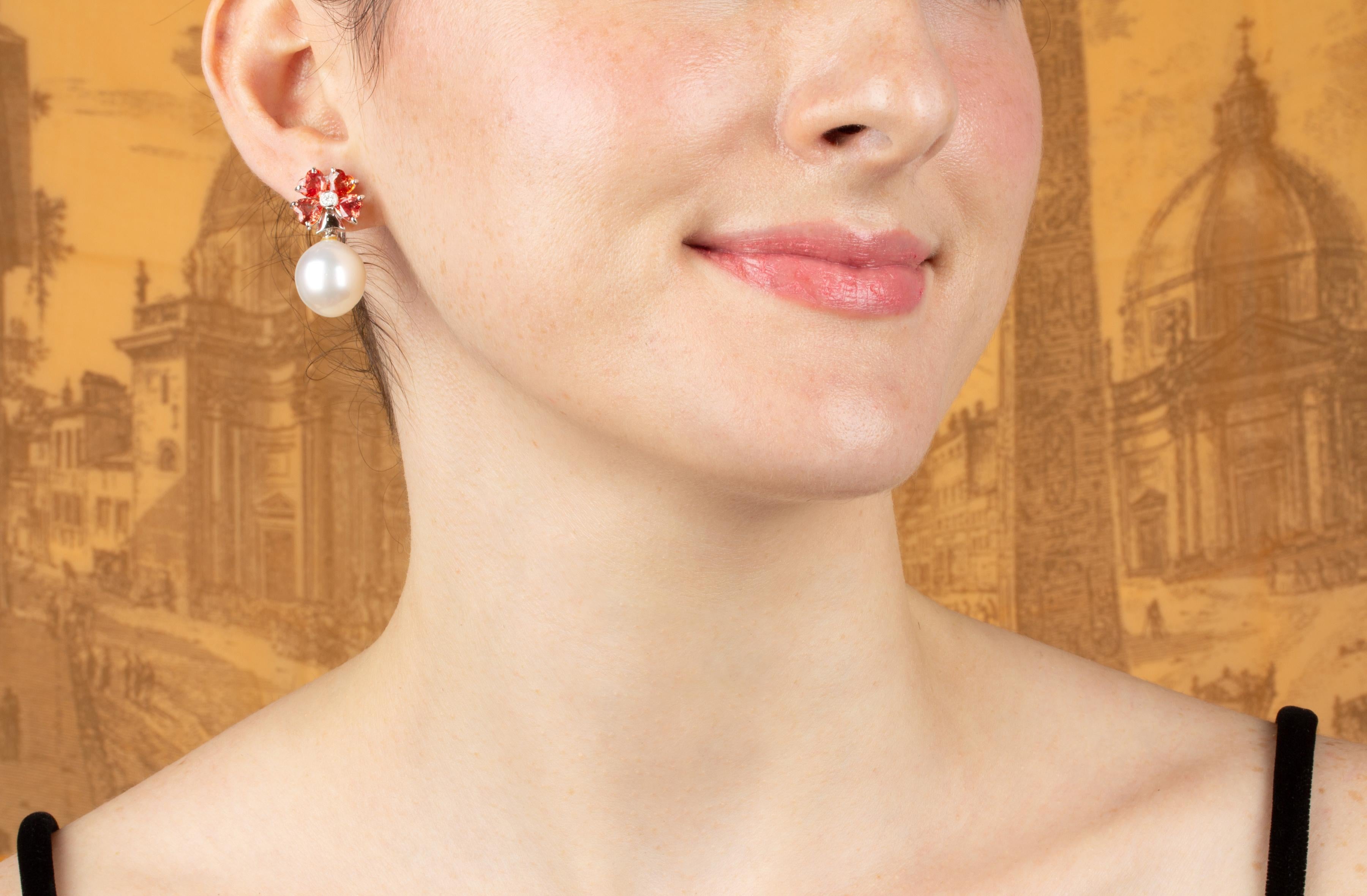 The pearl and sapphire earrings features a flower design on the ear with 6.98 carats of heart shape faceted orange sapphires. The tops suspend 2 South Sea pearls of 15mm diameter. 0.20 carats of round diamonds complete the design.
All of our pearls