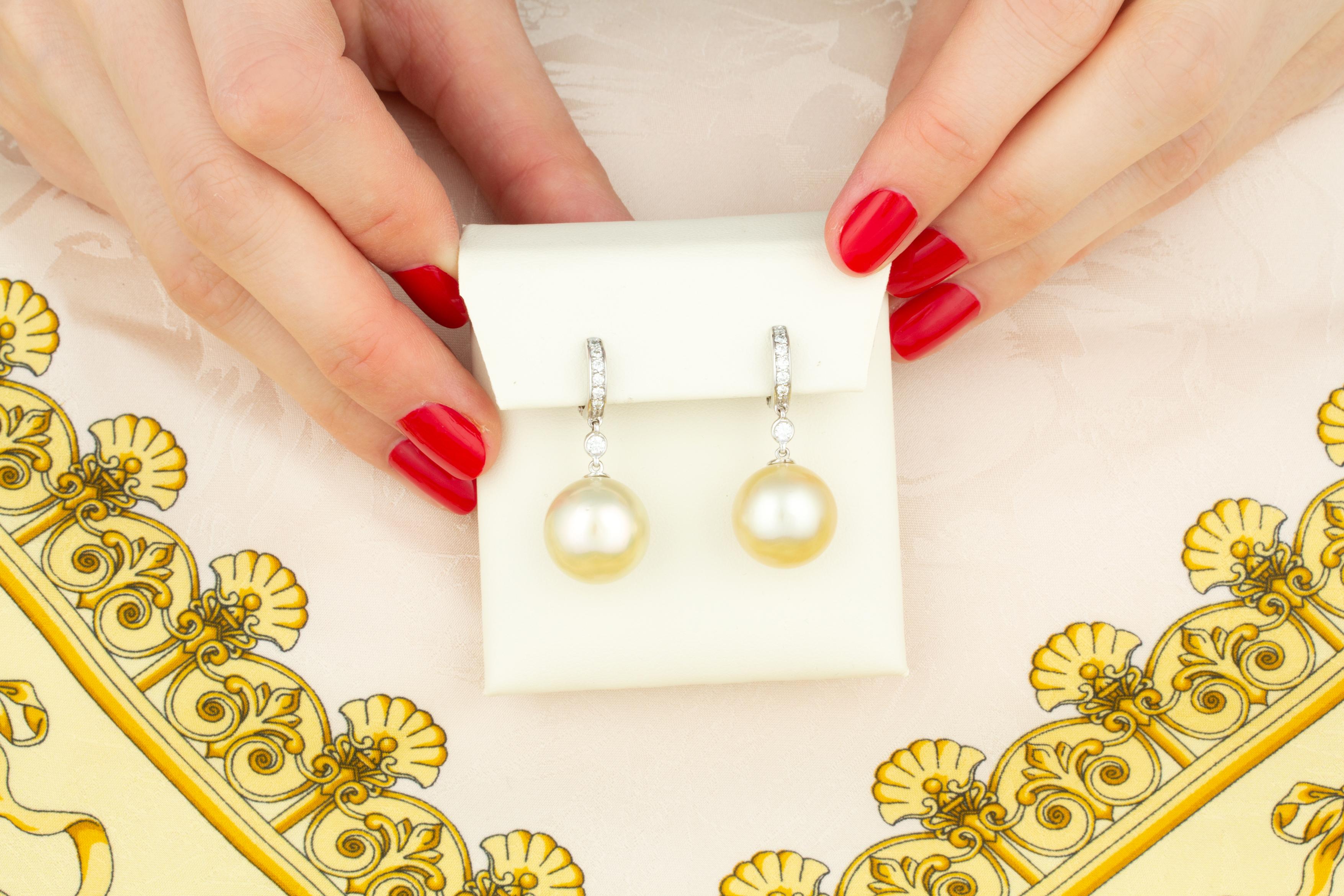 Les boucles d'oreilles pendantes en perles d'or et diamants sont composées de deux perles de 14,5 mm de diamètre, d'une nacre de qualité, d'un bel éclat et d'une belle couleur champagne.
Les perles sont suspendues à des anneaux sertis de diamants