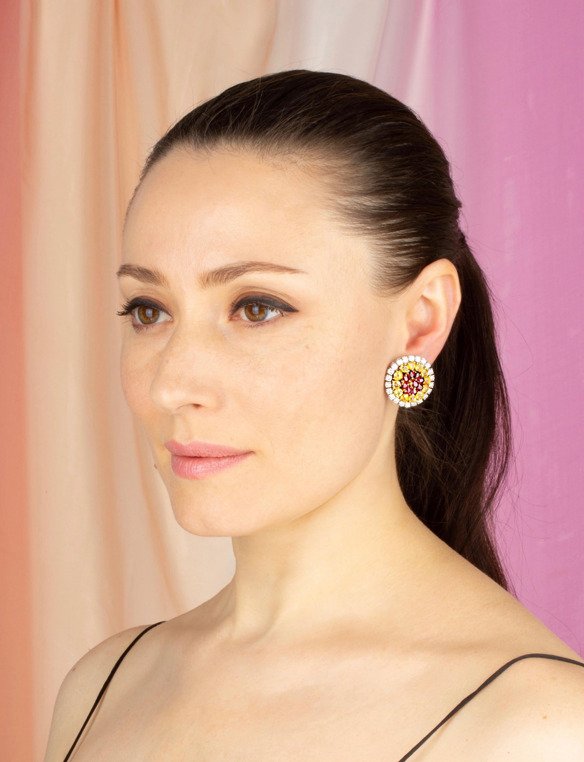 The sapphire ruby and diamond earrings feature a central flower of faceted rubies (6.08 carats) surrounded by a crown of calibrated yellow sapphires (approximately 10 carats). The colored stones are all of crystalline brilliant color. The design is