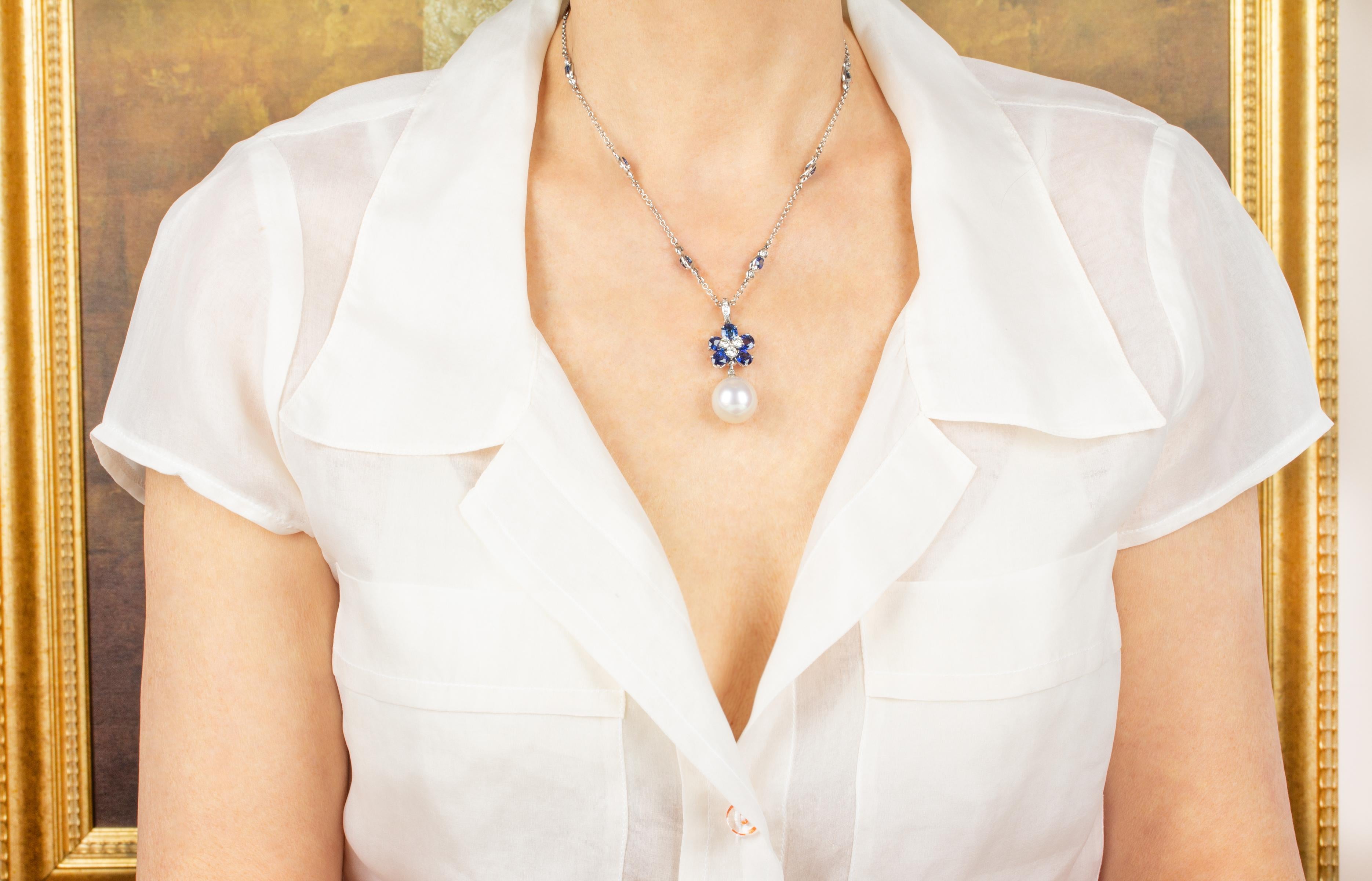The blue Ceylon sapphire pendant necklace features 5 faceted blue oval cut sapphires with a diamond center suspending a 16 x 17mm South Sea pearl. The 1.75” pendant is accompanied by a 16” 18 carat gold chain decorated with 8 blue sapphire motifs