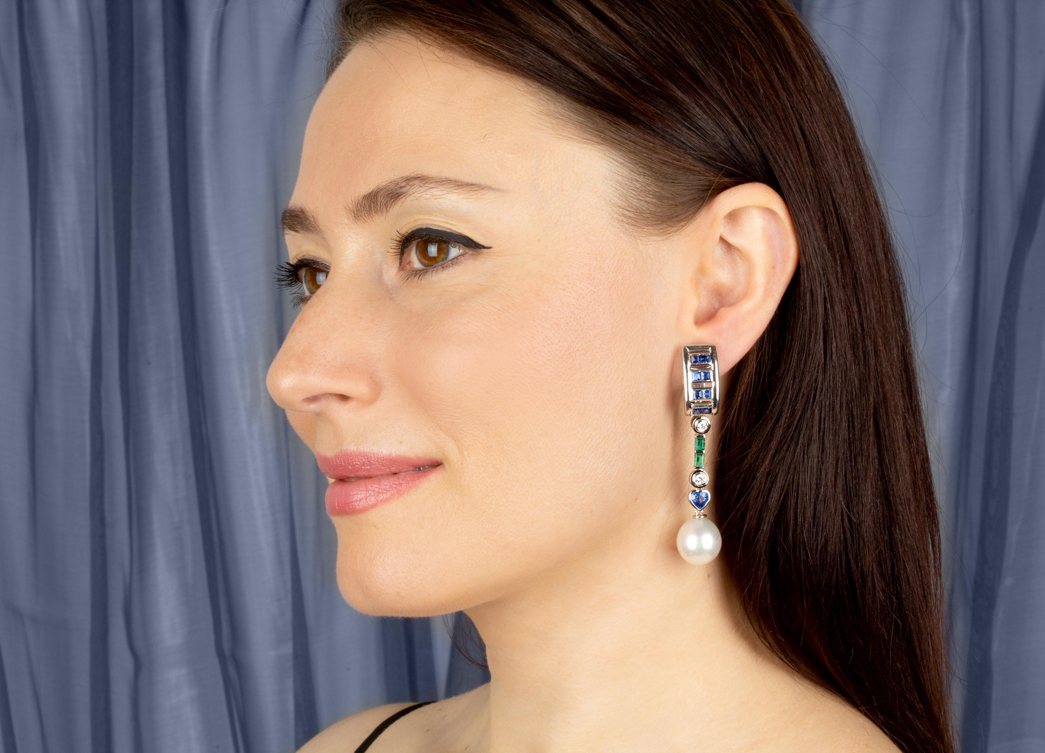 The sapphire and pearl earrings features a hoop-like design on the ear set with faceted blue sapphires. The tops suspend an articulated column set with round diamonds, emeralds, and heart shape sapphires. The total weight of blue sapphire is 4.02,