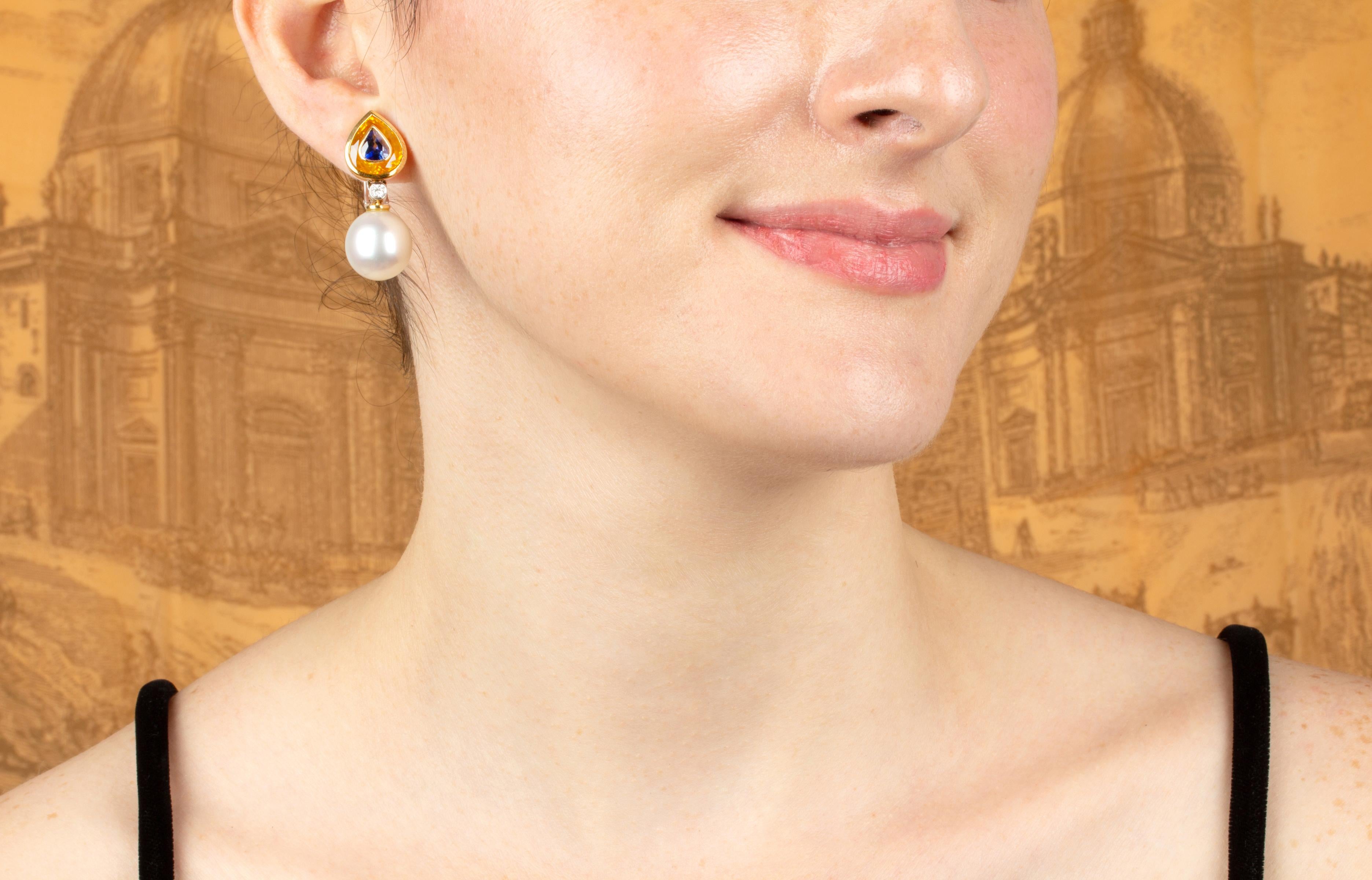 The sapphire and pearl earrings feature two faceted pear shape blue sapphires encrusted into two larger faceted yellow sapphires, a rare technical feat. (Total weight of sapphires is 15.51 carats). The tops suspend –via a round diamond- a pair of