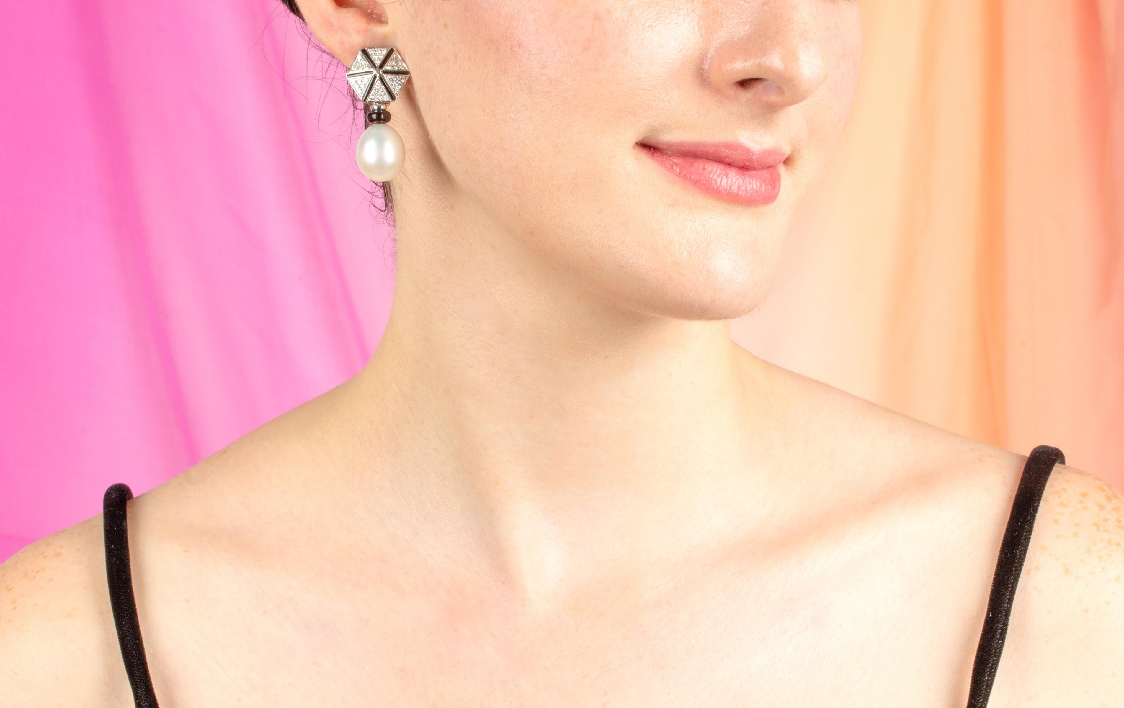 Die Ohrringe mit Südseeperlen und Diamanten haben ein geometrisches Design mit schwarzem Onyx und Diamanten, an denen zwei ovale Perlen von ca. 14 x 16 mm hängen. Die Ohrringe haben einen ausgeprägten Art-Déco-Look. Die unbehandelten Südseeperlen