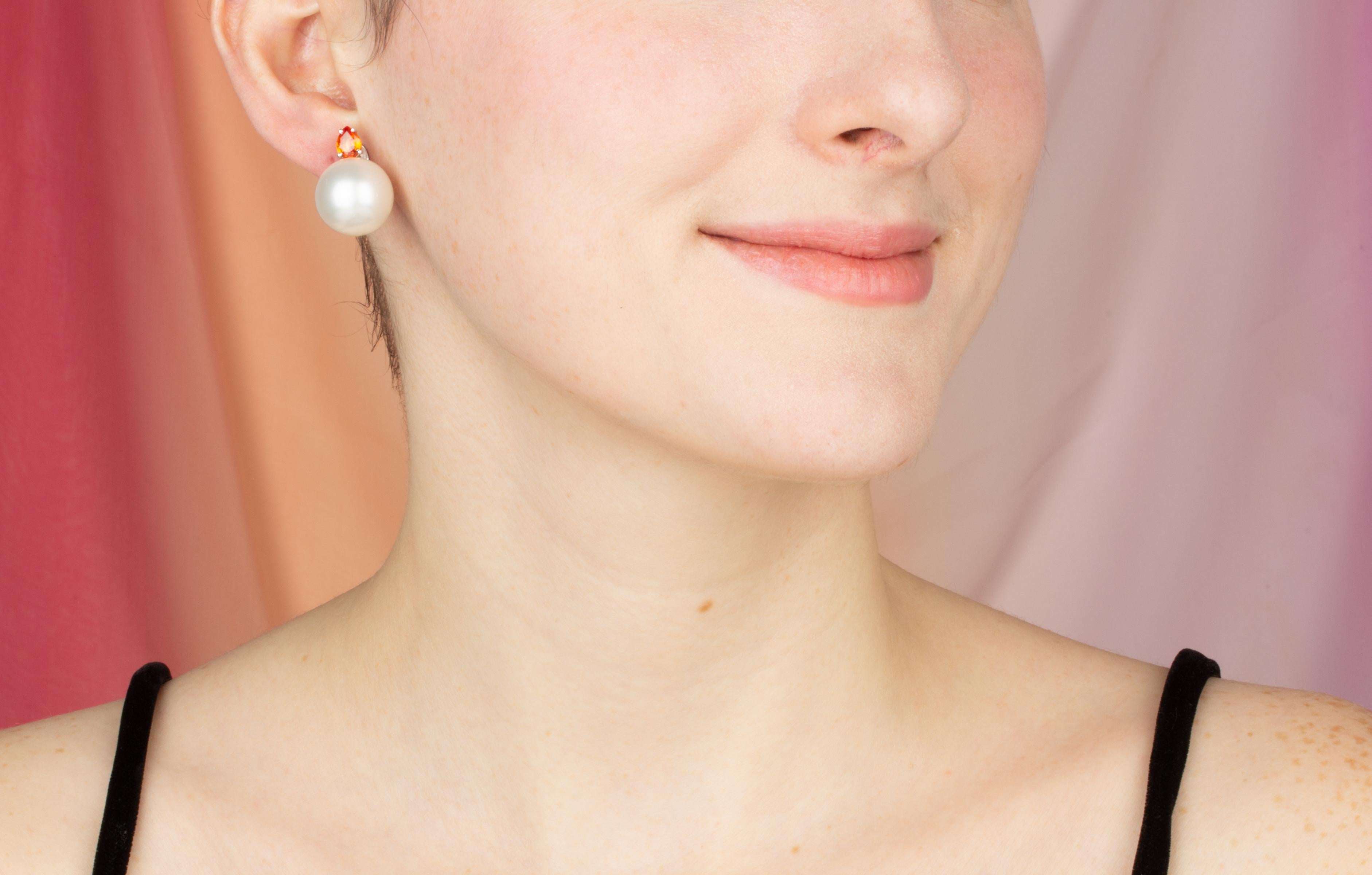 The South Sea pearl and sapphire earrings feature two large 15.5mm diameter pearls originating from the waters of Northwestern Australia. 
The design is complete with two faceted drop shape orange sapphires of brilliant color (0.72 carats).
All of