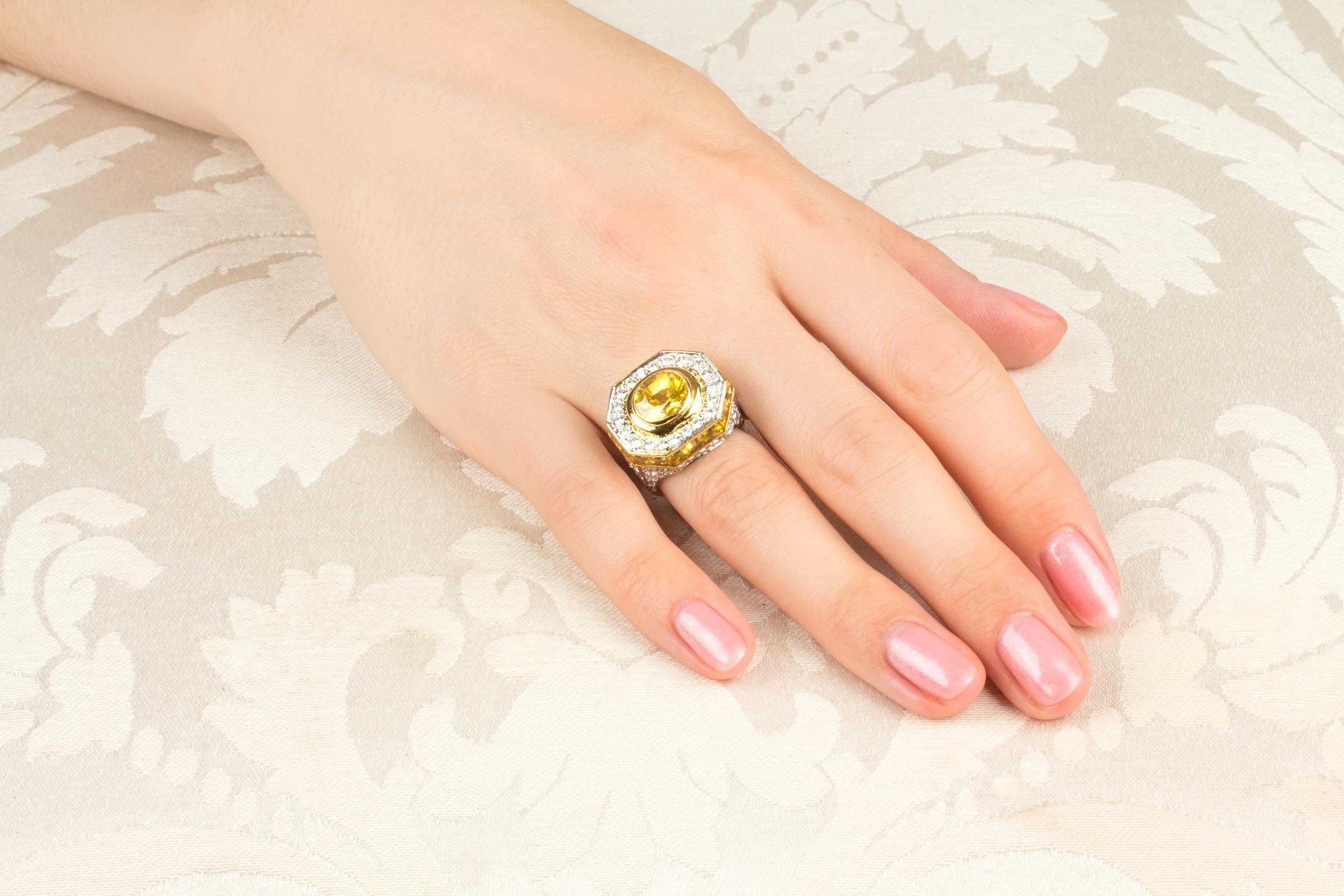 Este anillo meñique de zafiro amarillo y diamantes presenta un zafiro facetado de talla oval de color brillante (3,20 quilates) rodeado por una corona de diamantes redondos. El diseño en forma de cúpula está circunscrito por una hilera de zafiros