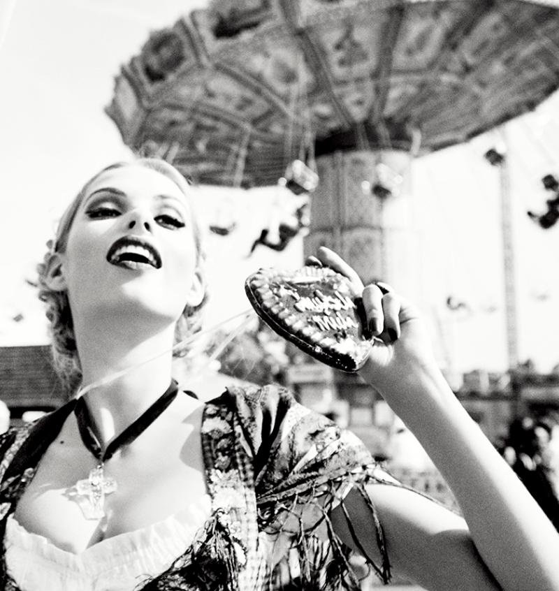 Zwei Models in traditioneller deutscher Kleidung stehen zwischen Karussells und halten Lebkuchenherzen, fotografiert von Ellen von Unwerth 2015 für ihre Serie 