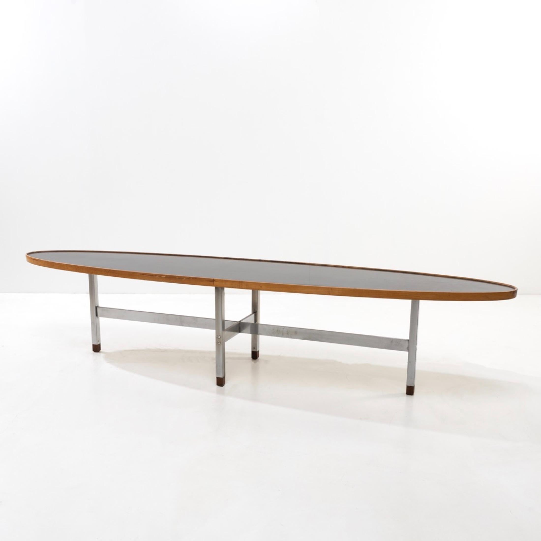 Large elliptical-shaped coffee table, the black laminate (formica) top surrounded by wood.
The top rests on four stainless steel legs with double spacers assembled by screws receiving wooden heels.