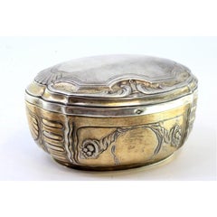 Elliptical silver box with reliefs surrounding monogram cards, gold interior