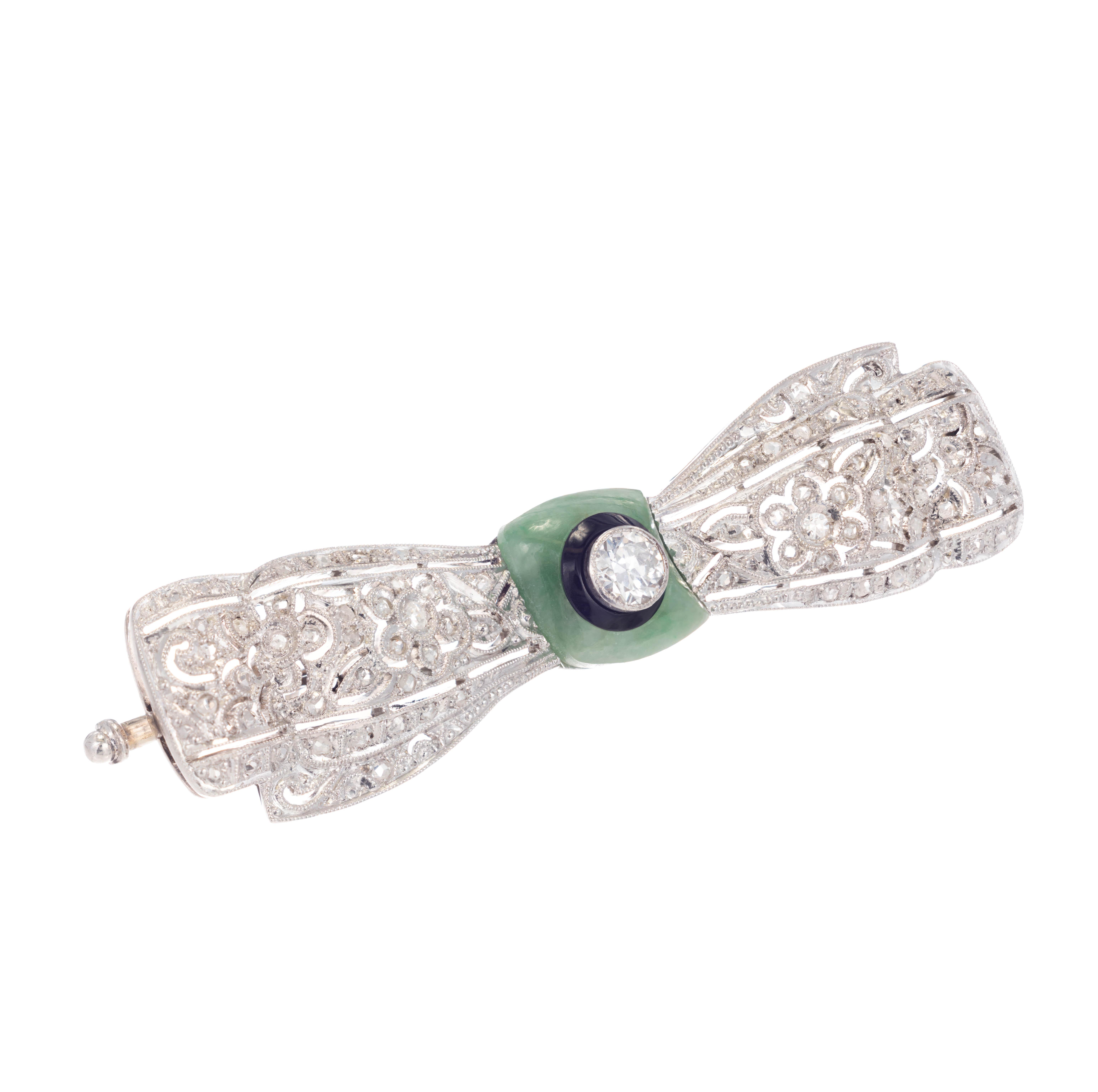 Art Deco Ellis Brothers diamond, jadeite and onyx bow style brooch. An Old European cut diamond is bezel set and inserted into an onyx ring which is then set into a wavy square. Jadeite jade at the center. The lattice and floral bow design is