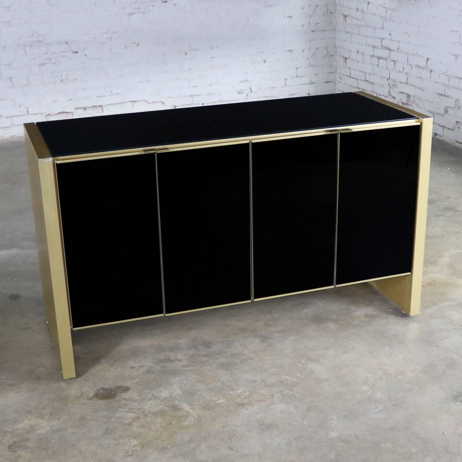 Elegant small credenza or server cabinet attributed to Ello in black glass and gold anodized and brushed aluminum. It is in wonderful vintage condition. There are a few nicks and dings in the aluminum laminate and there is one small spot on a glass