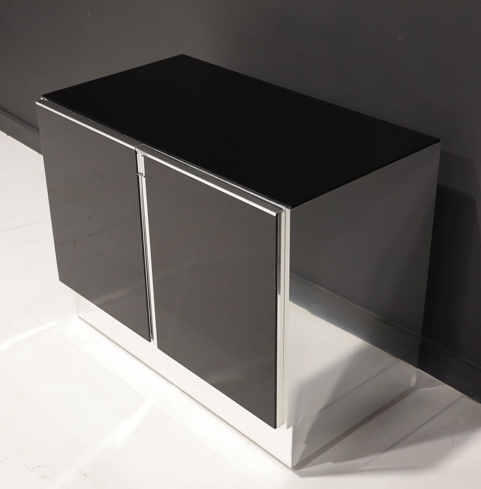 Schwarzer Glasschrank Ello aus den 1970er-Jahren mit verchromter Zierleiste. Schwarze Glasplatte und -front mit verchromten Beschlägen und Seiten. Öffnet sich und gibt ein einzelnes Regalfach frei.