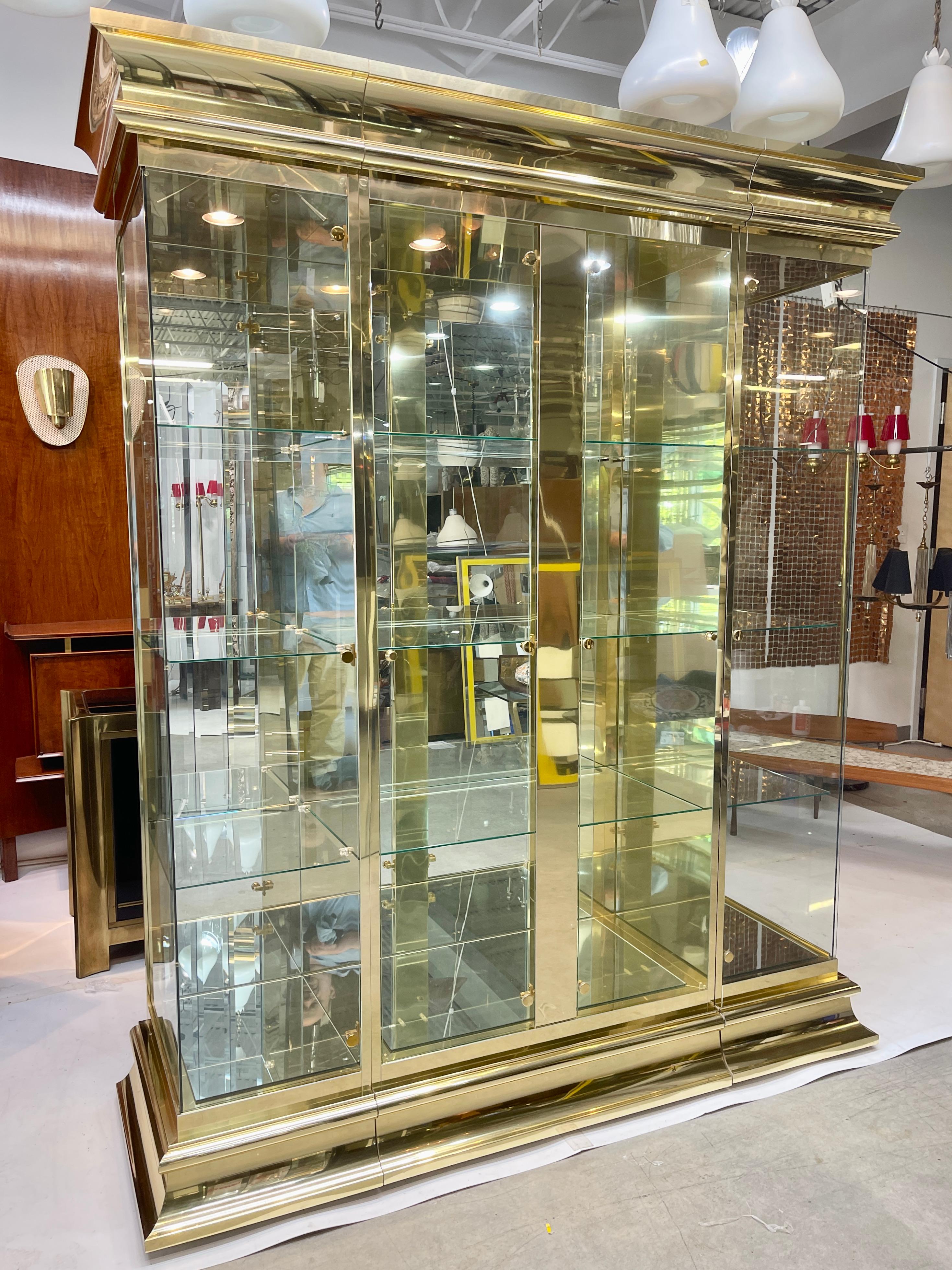 Brass and mirror three section illuminated curio display showcase designed by O. B. Solie in 1986 for Ello Furniture Manufacturing Corp. of Rockford, IL as part of the LaCage Collection. 
Nine glass shelves with engraved plate slots. Mirror floors