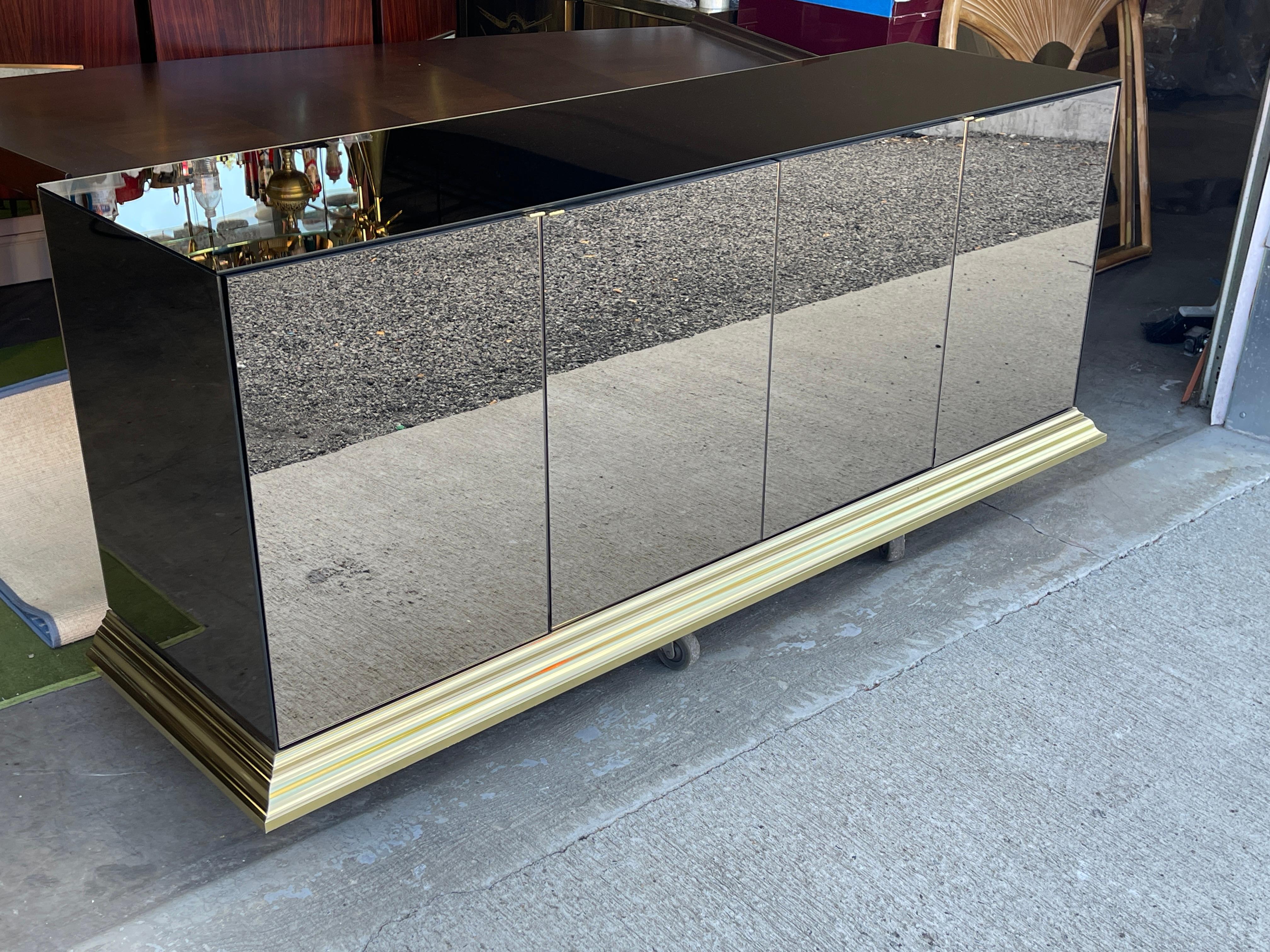 Minimalismus trifft Hollywood-Glamour. 
Bronzefarbenes, spiegelverkleidetes, viertüriges Sideboard auf einem Sockel aus gegossenem Messing.
Diskrete Türgriffe machen dieses große Teil praktisch unsichtbar - wie das Flugzeug von Wonder Woman!
Obwohl