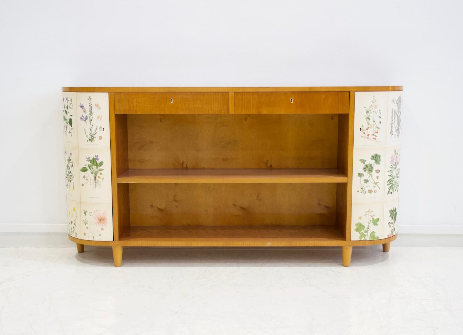Cabinet / bookcase veneered with elm wood from circa 1940's. Two long shelves and two drawers on top, sides with doors behind which are shelves. Later covered with flower illustrated paper. The prints are from the book 