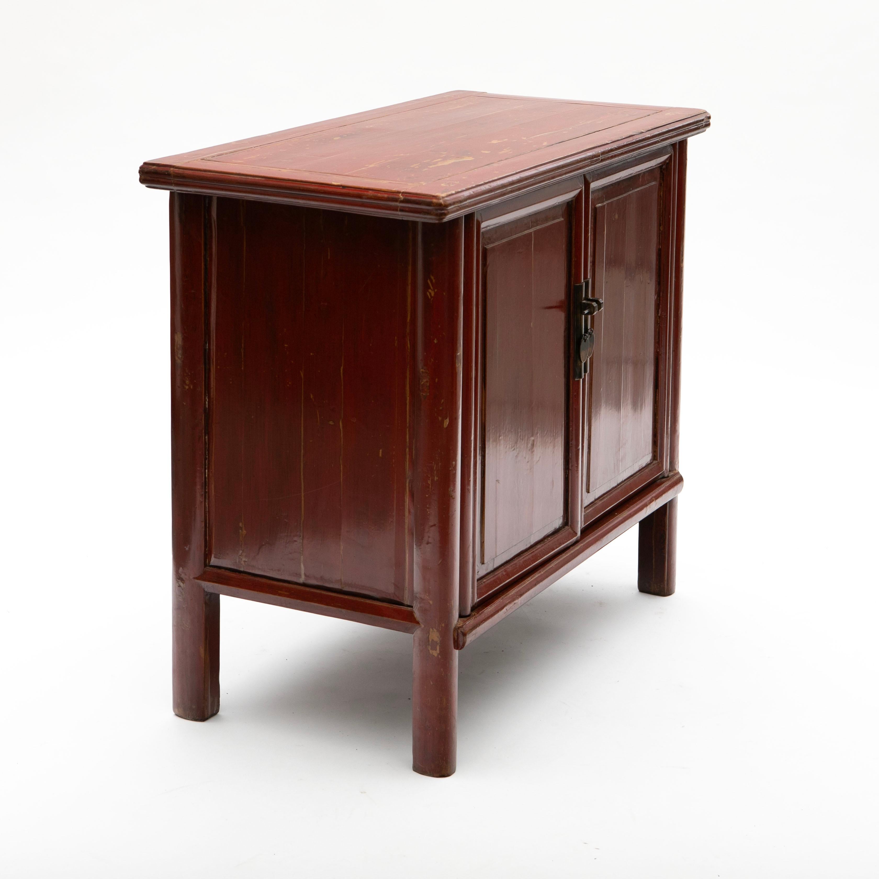 This well-preserved Ming-style cabinet, dating from around 1860.
It is crafted from elm wood and retains its original red lacquer, which has developed a beautiful natural patina over time.
The cabinet features two paneled doors framed by profiled