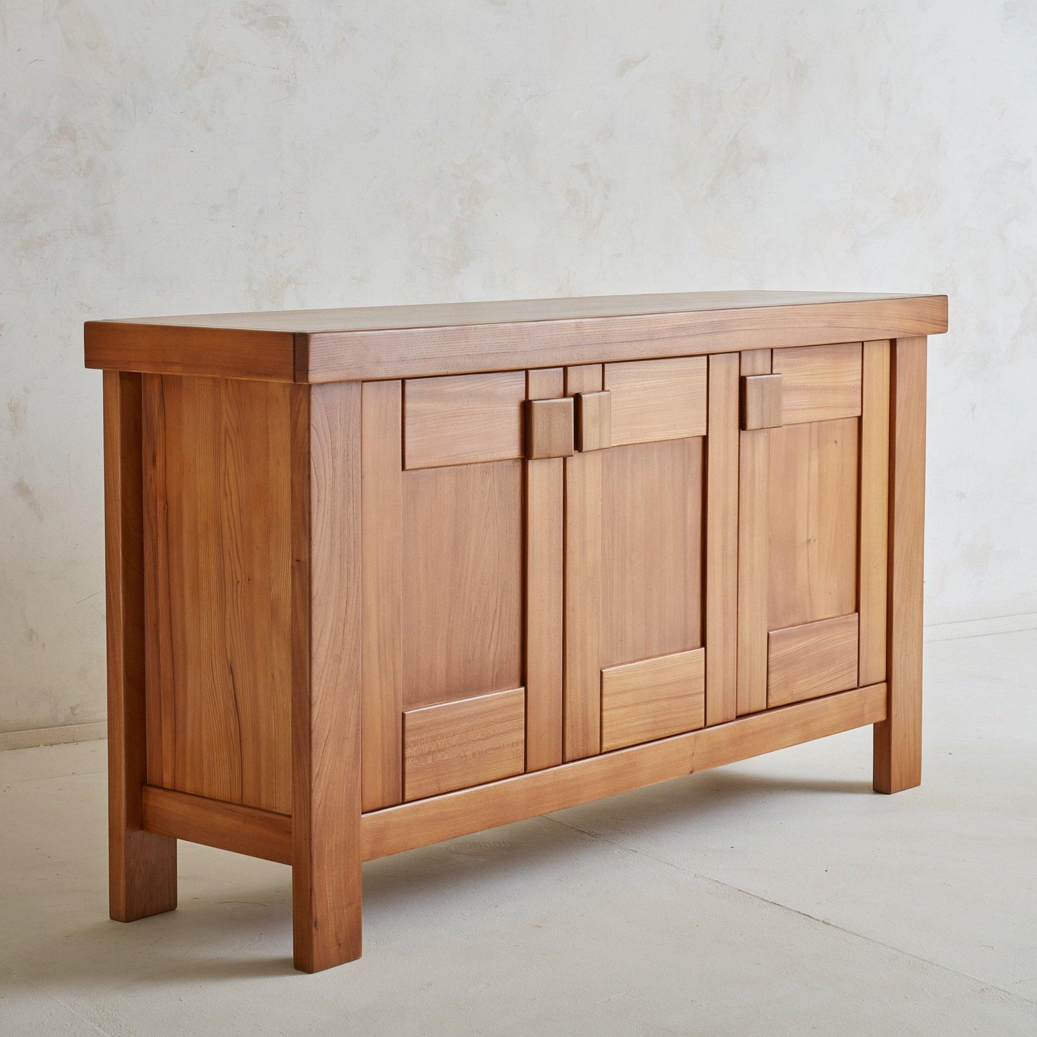 A 1970s French sideboard attributed to Maison Regain. This piece features beautiful craftsmanship; it was constructed with subtly grained elm wood that highlights the sleek lines throughout. Three doors with block pulls open to reveal a center shelf