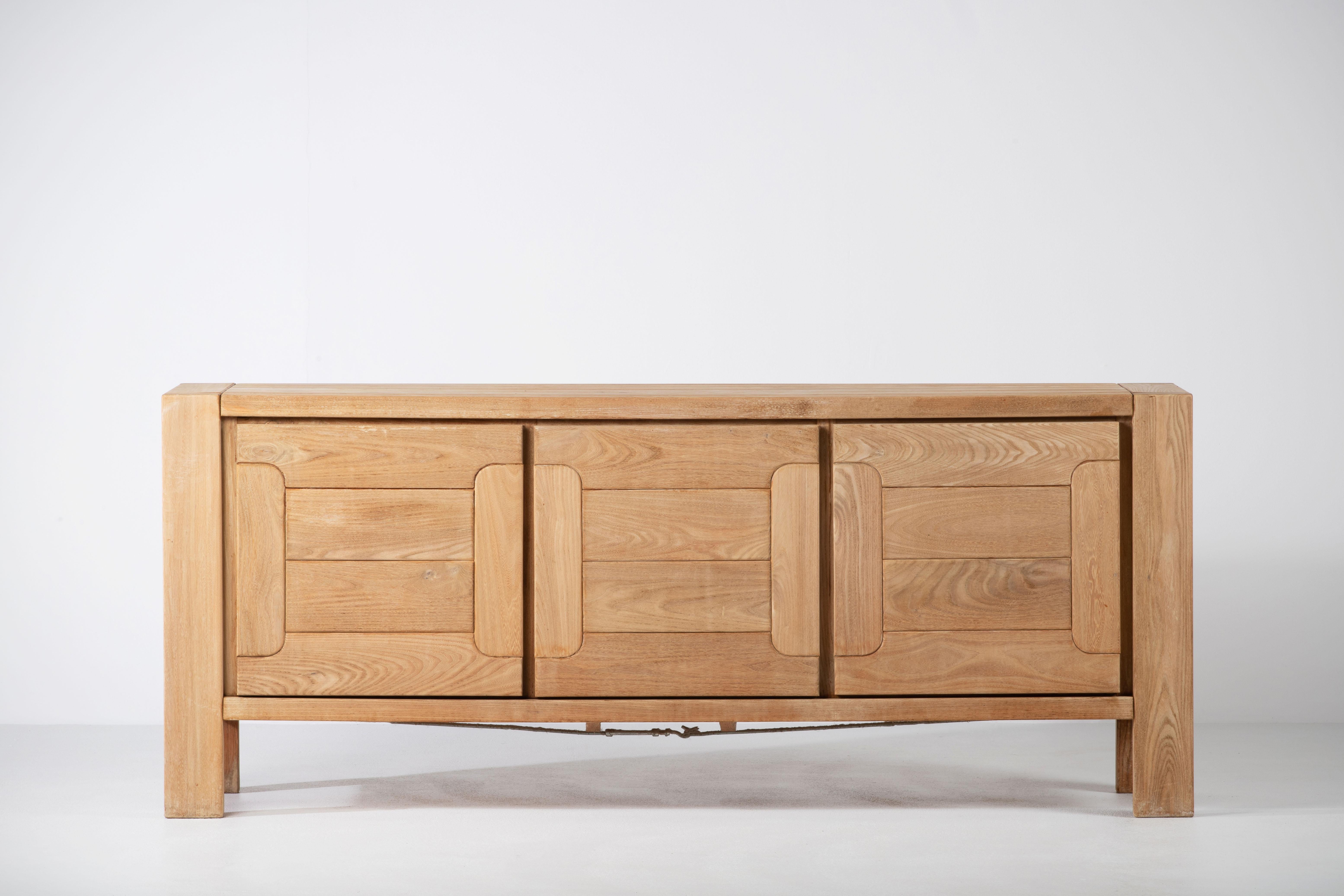 This impressive sideboard is attributed at Maison Regain, France in the late 1970s. The sideboard is made in solid elmwood and has a double door on the left with two beautifully crafted, sculptural handles. 
The wooden connections on the top, the