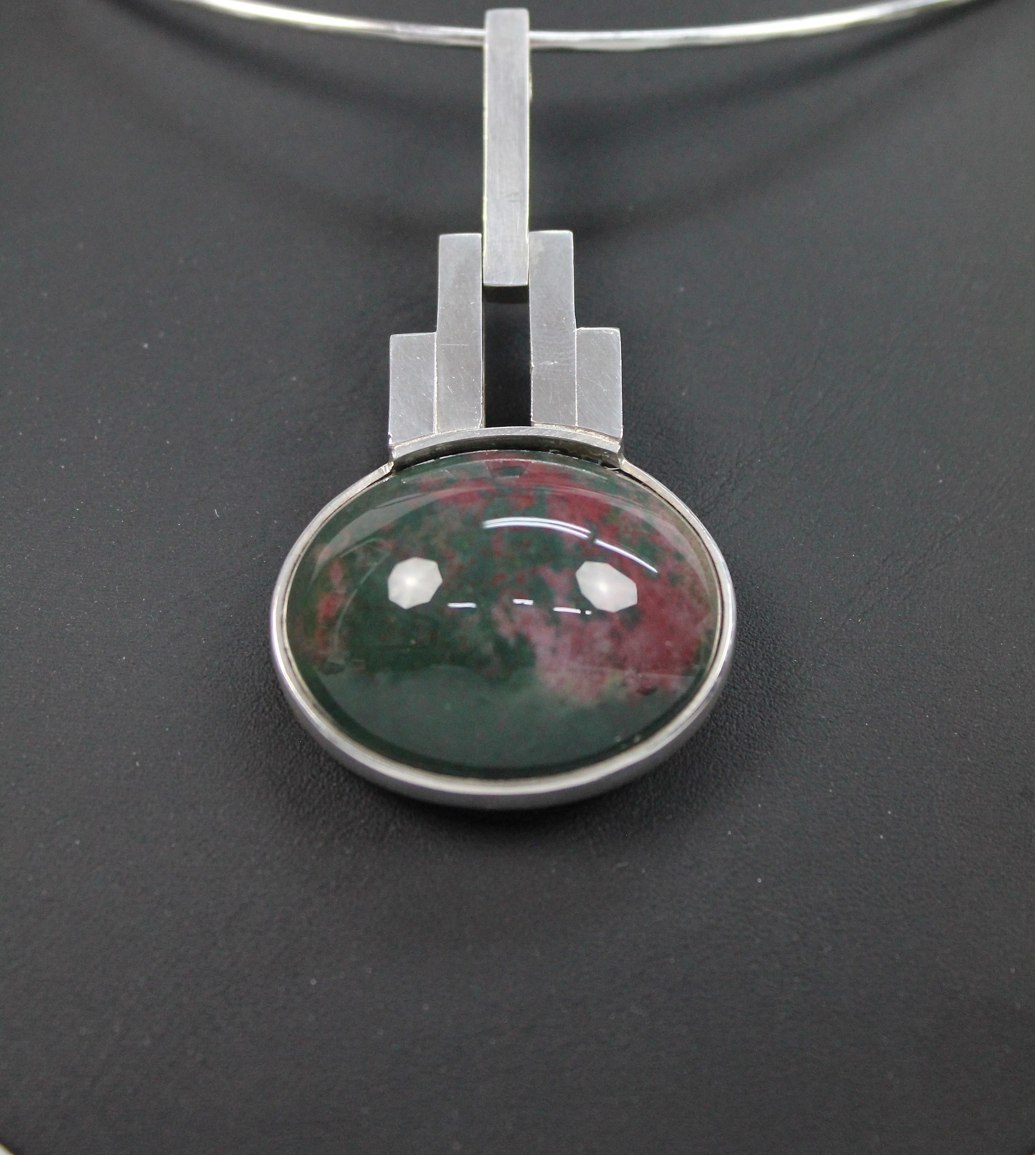 A modernist necklace by Elon Aronhill, Malmö Sweden 1967.
Both necklace and pendant are in sterling silver.
The pendant is set with a large cabochon cut bloodstone or Heliotrope.

Very nice vintage condition. No issues.

The diameter of the ring is