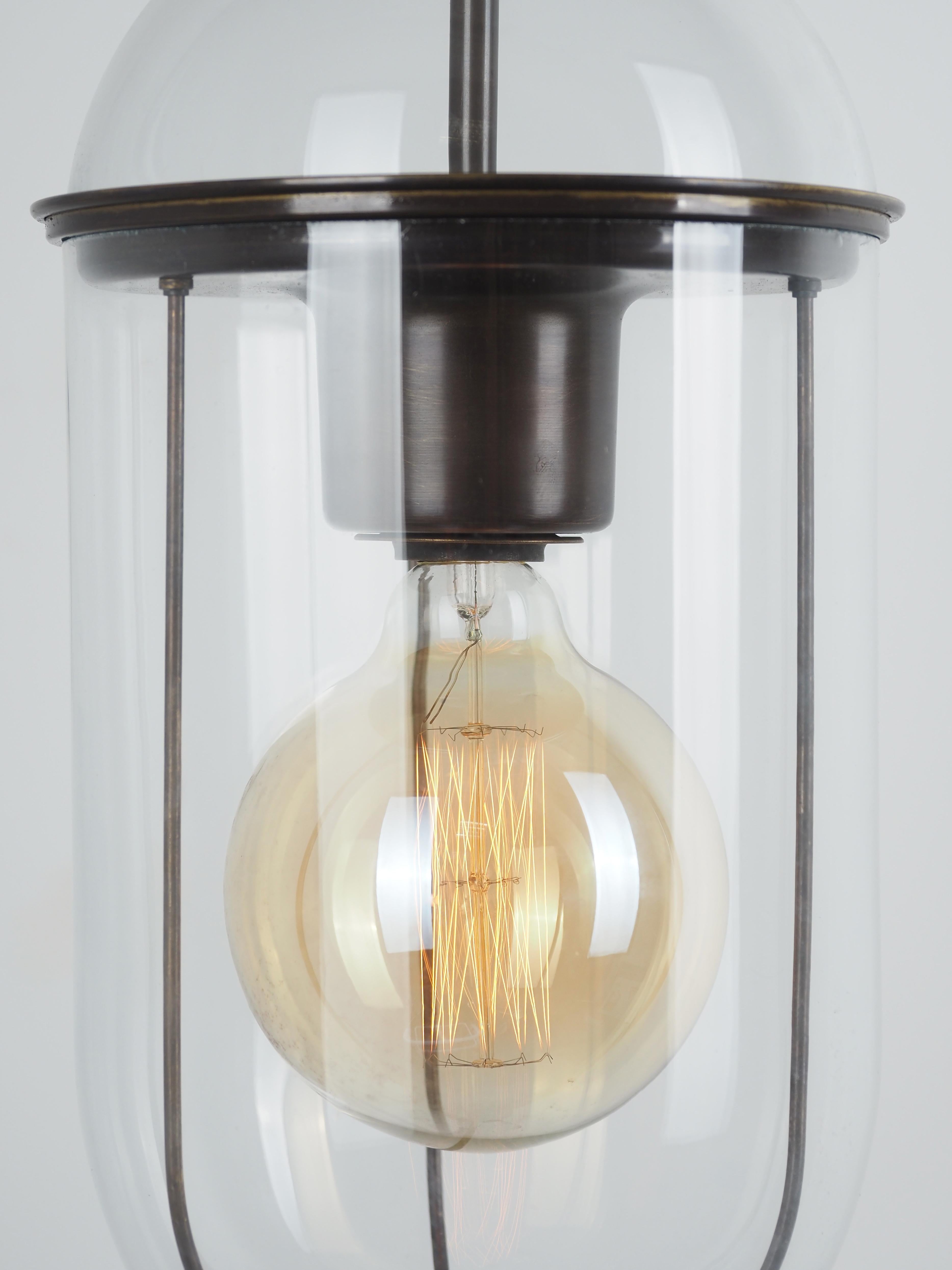 Contemporary Italian elongated shape pair of clear glass pendent lights. 
Two pieces of glass separated by a horizontal ring which holds the single light socket.
A bronze cage lines the interior.
Lower piece of glass twists off for easy bulb