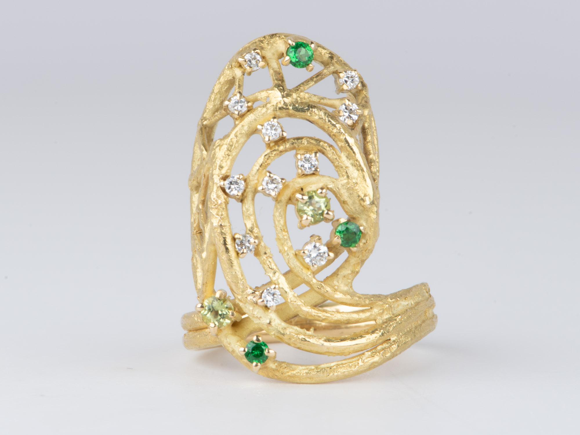 This Modernist Design Ring is truly extraordinary. It has a unique texture that nicely complements the cluster of diamonds and bright green and mint green garnets. The great finger coverage in luxurious 18K gold will make you stand out from the