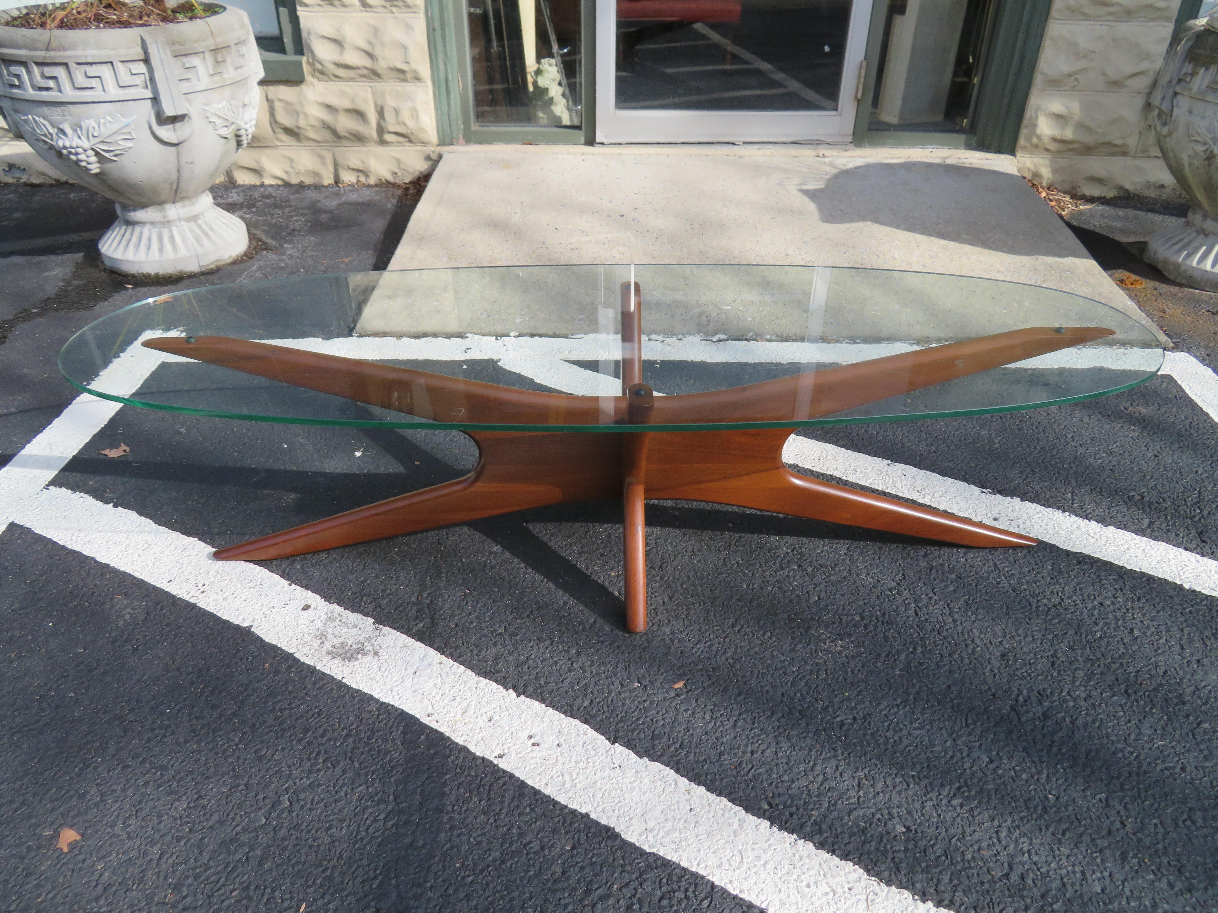 A super mod cocktail table with an elongated interlocking boomerang form walnut Jax base supporting an oval glass top. Model. no. 893-TGO by Adrian Pearsall for Craft Associates, American, circa 1960. This piece is in fabulous condition, the base