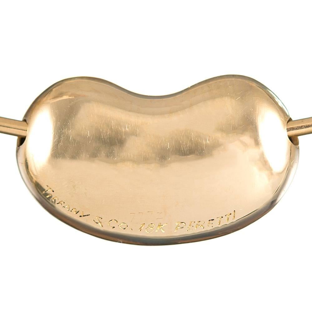 The Golden wire measures 5 inches in diameter, sitting so it just grazes the collarbone. An extra-large 1 inch long high-polished bean slides to and fro. Signed Elsa Peretti for Tiffany & Co.