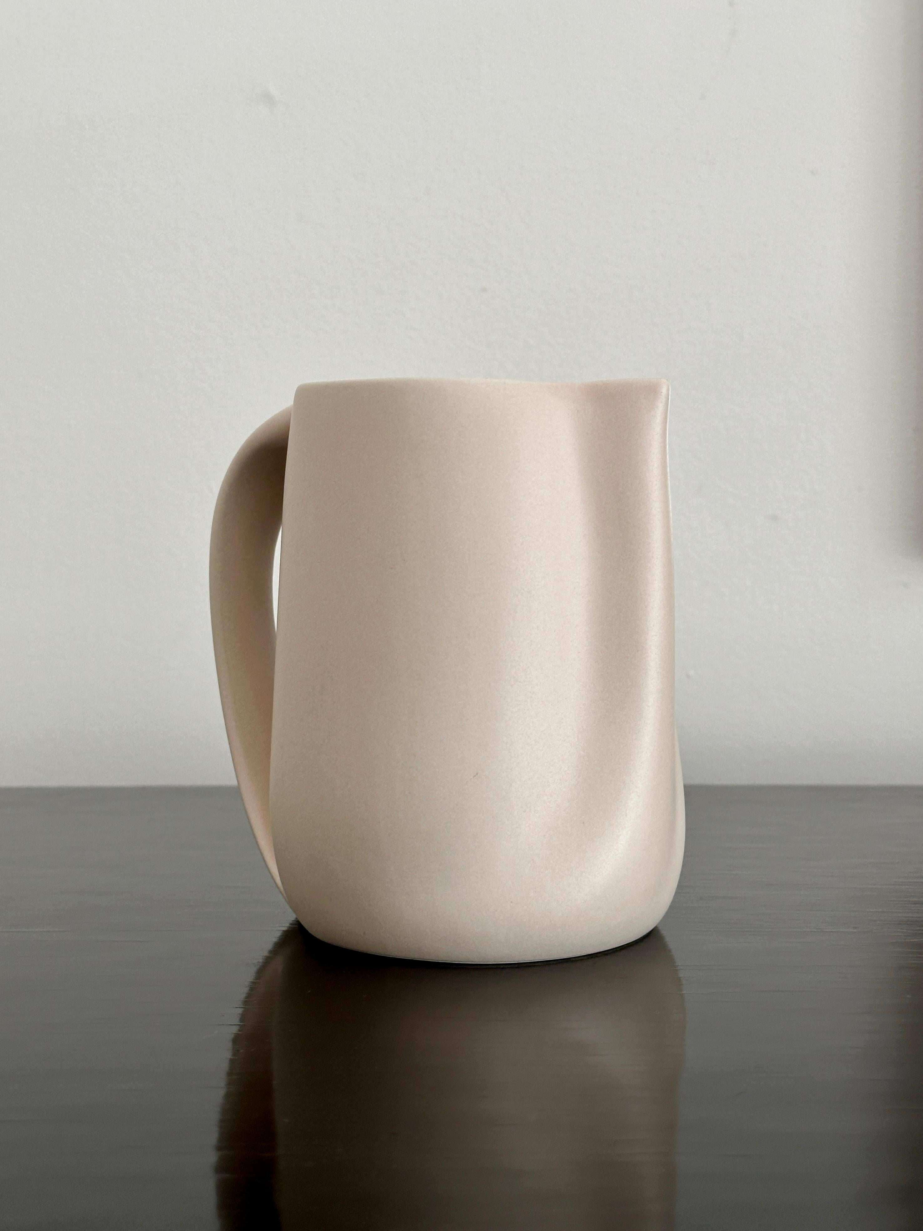 A small water pitcher designed by Elsa Peretti in the 1960’s - 1970’s for Tiffany & Company. The pitcher has a matte putty tinted outer glaze and a shiny cream colored glaze on the inside. The pitcher is approximately 5 ½ inches tall and 9 inches at