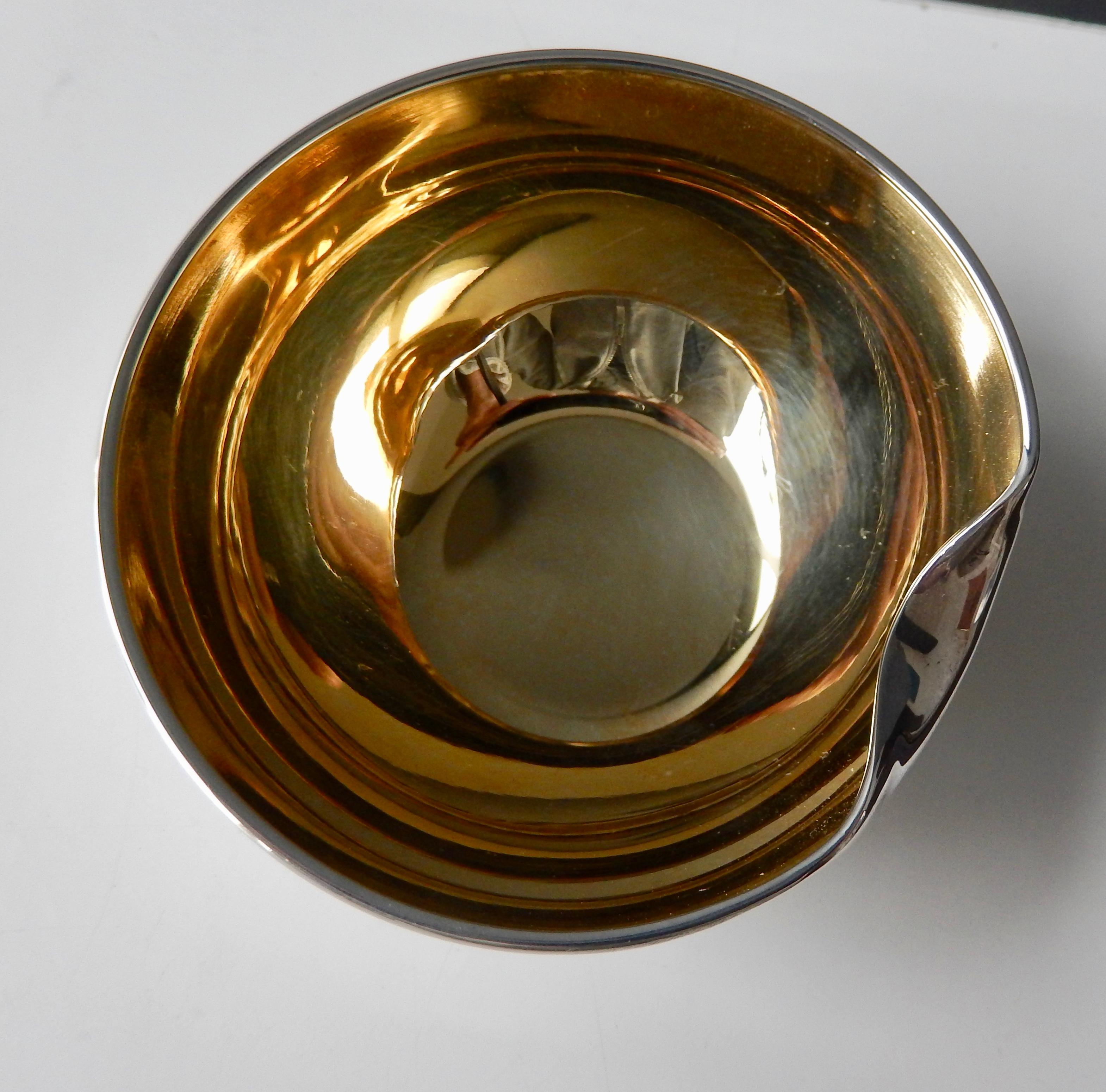 A small, luxurious sterling silver bowl with a gold vermeil interior by the well-known Tiffany & Co. designer Elsa Peretti. The bowl's simple sculptural shape, resembling a 