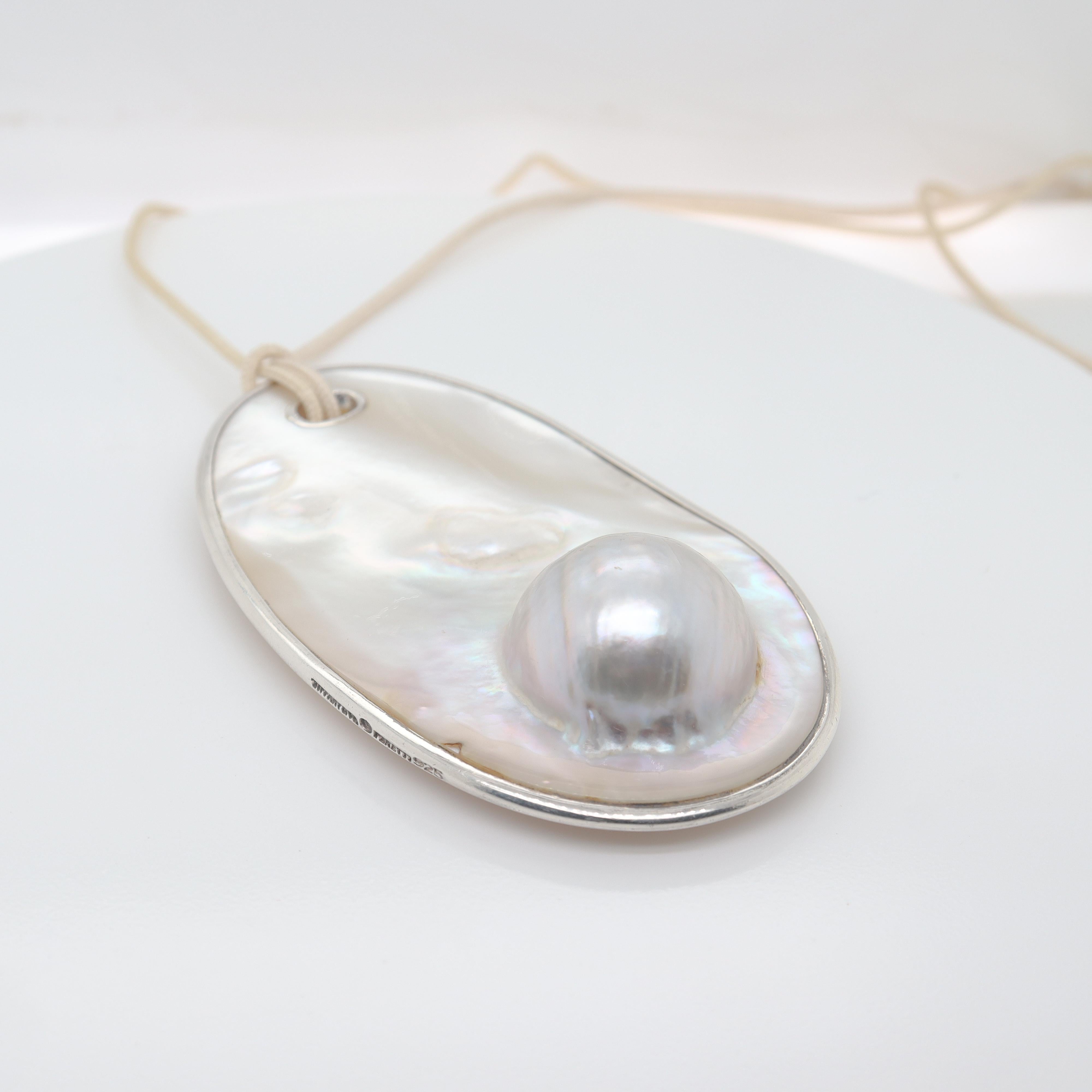 A fine silver & blister pearl necklace.

Designed by Elsa Peretti for Tiffany & Co. 

Comprised of a large blister pearl disc mounted with a sterling silver rim and set with a silver eyelet. 

Together with a white nylon cord.

Simply wonderful