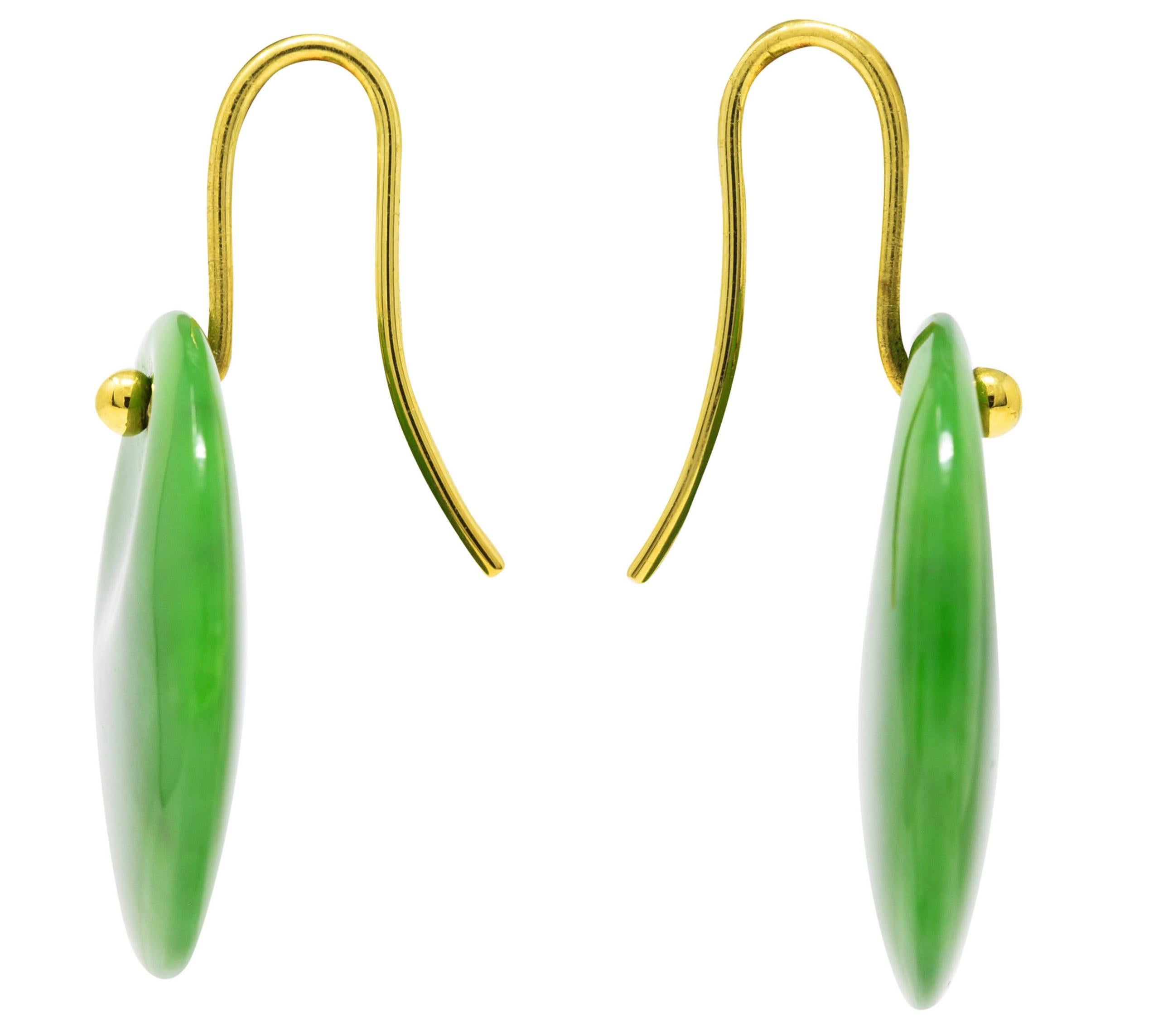 Earrings are designed as 25.0 mm round carved jade disks with circular contour. Translucent medium yellowish green with dark green mottling. Suspended from wire ear hooks terminating with gold beads. Stamped 750 for 18 karat gold. Signed Peretti