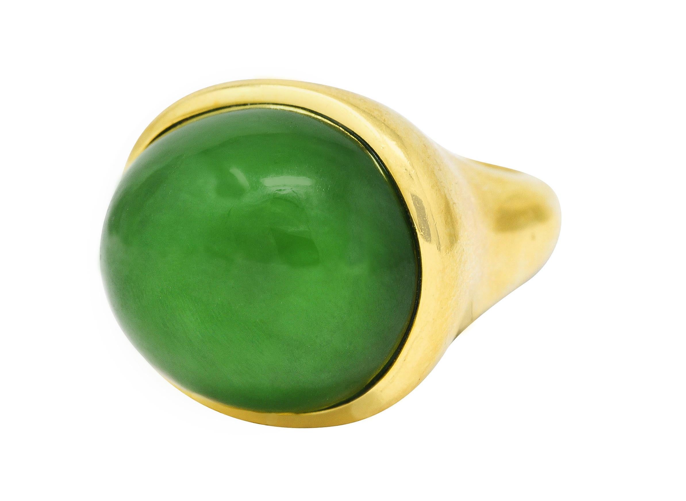 Ring centers a substantial oval jade cabochon measuring 16.5 x 19.5 mm. Opaque green with medium saturation and light green swirling. Bezel set with a curved wavy surround. With a contoured shank. Stamped 750 for 18 karat gold. Fully signed Elsa