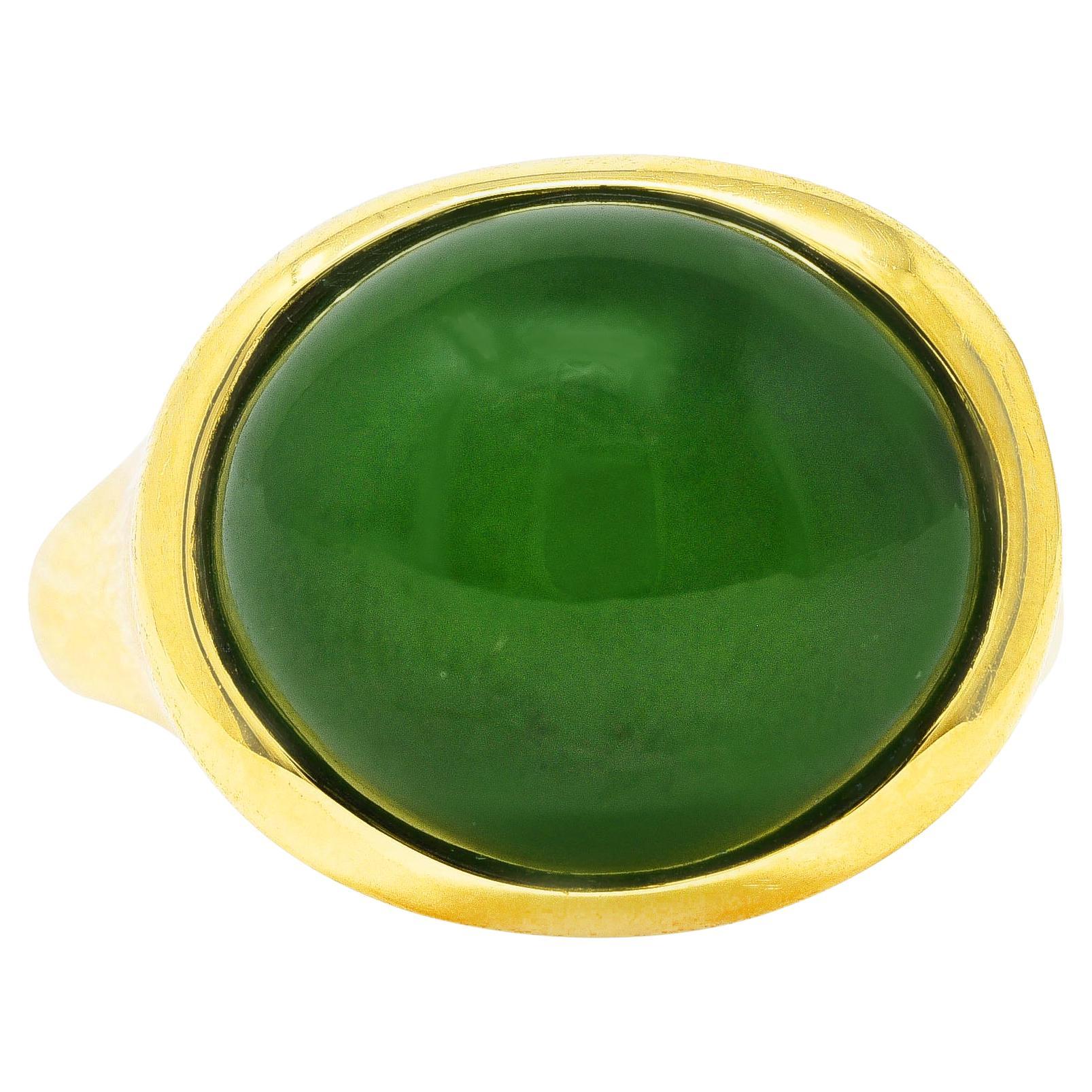 Ring centers a substantial oval jade cabochon measuring 13.0 x 15.0 mm. Opaque green with medium saturation and light green swirling. Bezel set with a curved wavy surround. With a contoured shank. Stamped 750 for 18 karat gold. 
Fully signed Elsa