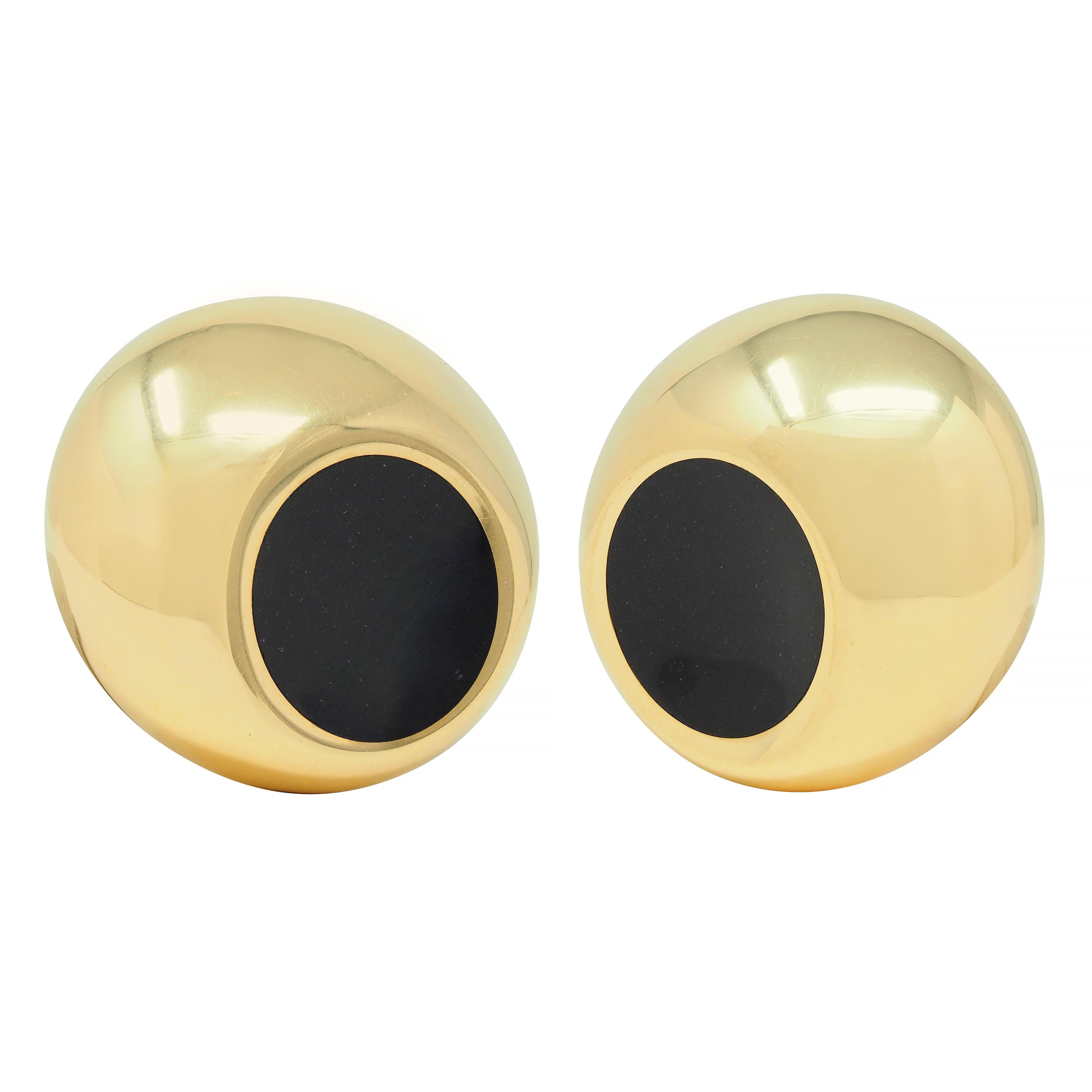 Designed as a round domed form with round imprint
Centering a 12.5 mm round inlaid tablet of onyx 
Opaque black with glossy finish 
With high polish gold finish
Completed by hinged omega back
Stamped with British assay marks for 18 karat
