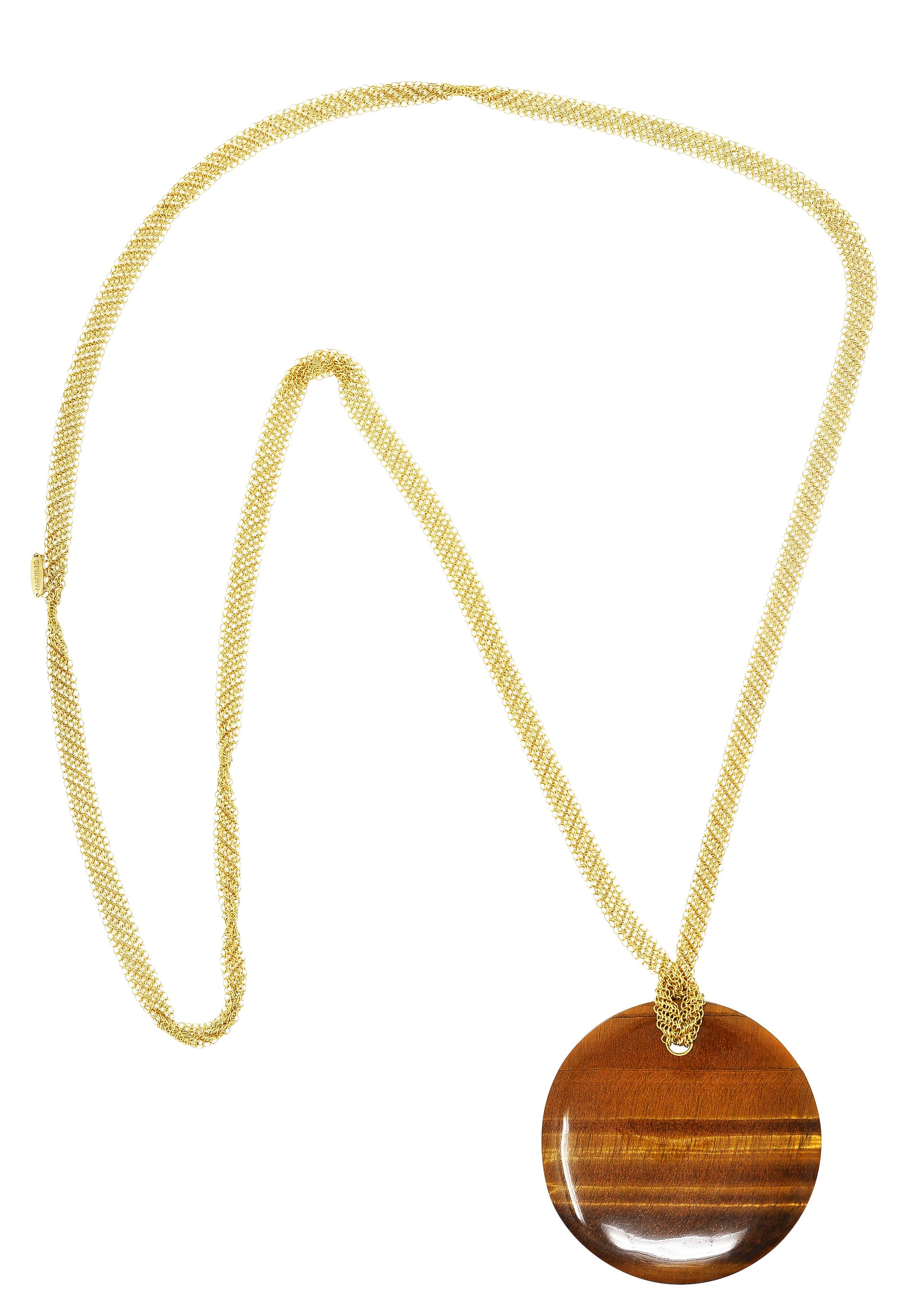 Featuring a substantial 50.0 mm touchstone pendant of tiger's eye quartz

Opaque with brown to yellowish orange banded color while exhibiting strong chatoyancy

Carved as a circle with a slightly concave impression

Suspending from a gold mesh