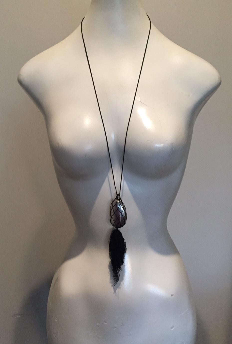 An unusual and rare form for the iconic Elsa Peretti bean, this large sterling silver bean is cradled in a hand woven black mesh bag. A large black tassel is suspended from the bag and a black cord completes the necklace. It is in excellent