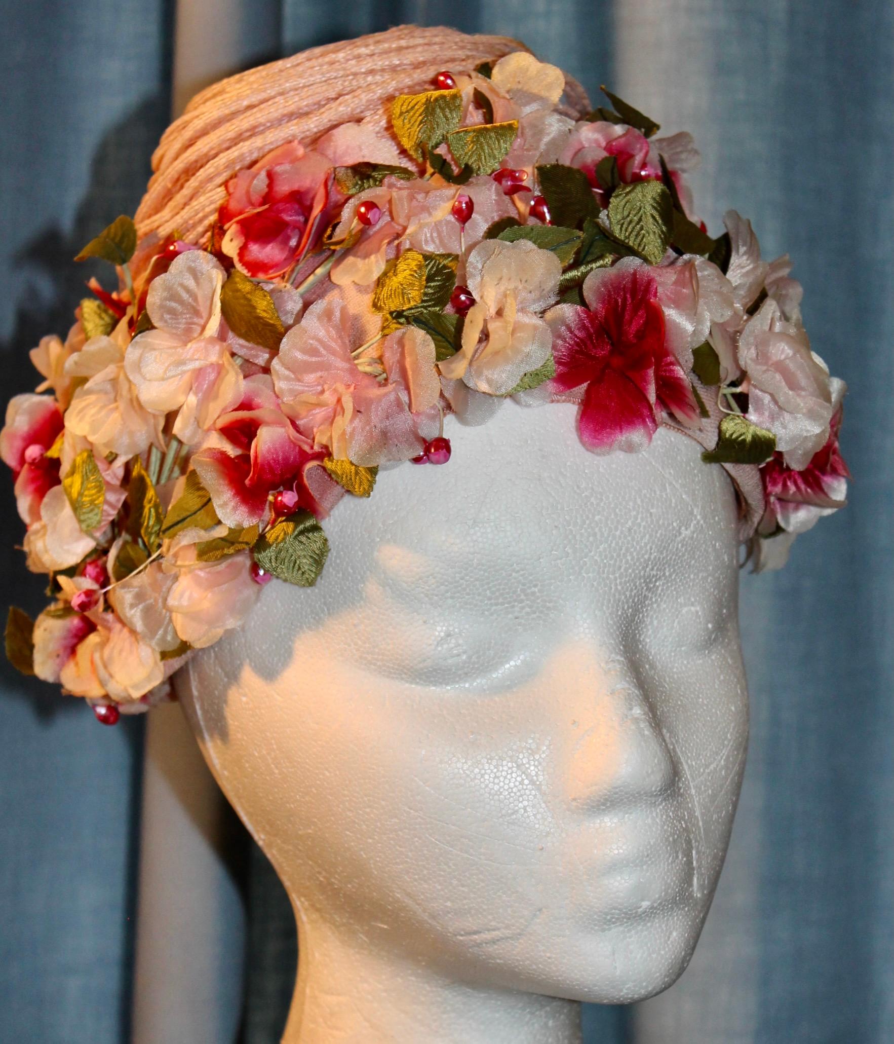 Elsa Schiaparelli Spring Hat with wreath of pastel silk flowers around the edge.
Wrapped straw, silken floss flowers, hand sewn attached to netting frame.
Topped with a pink swirling cord  'turban'.Outside measure 8