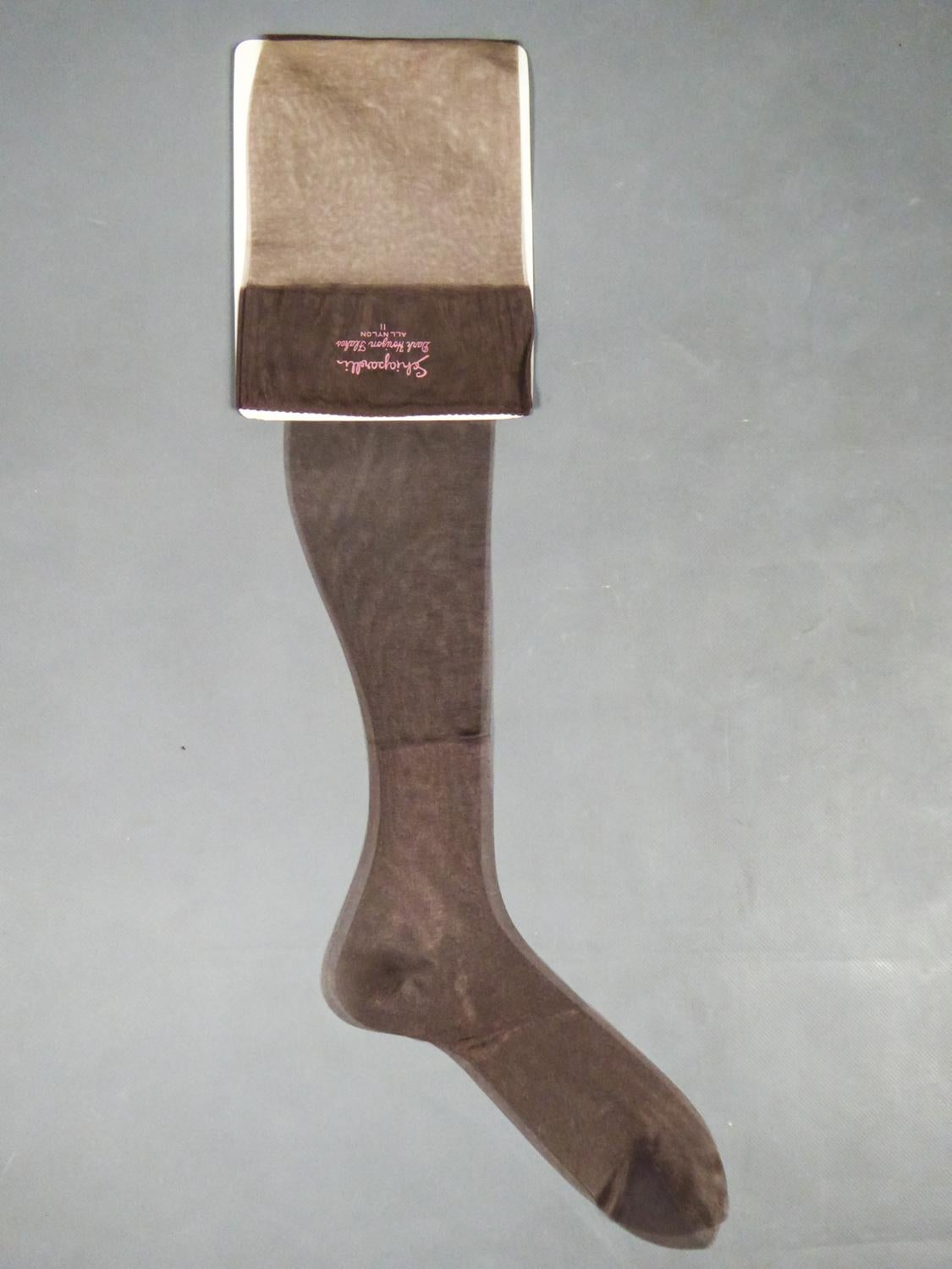 Circa 1958
États-Unis
Paire de bas par Elsa Schiaparelli dans sa boîte d'origine, comme neuf, pièce de collection datant de la fin des années 1950 aux États-Unis. Paire de bas en nylon marron avec le célèbre graphisme Schocking Pink indiquant
