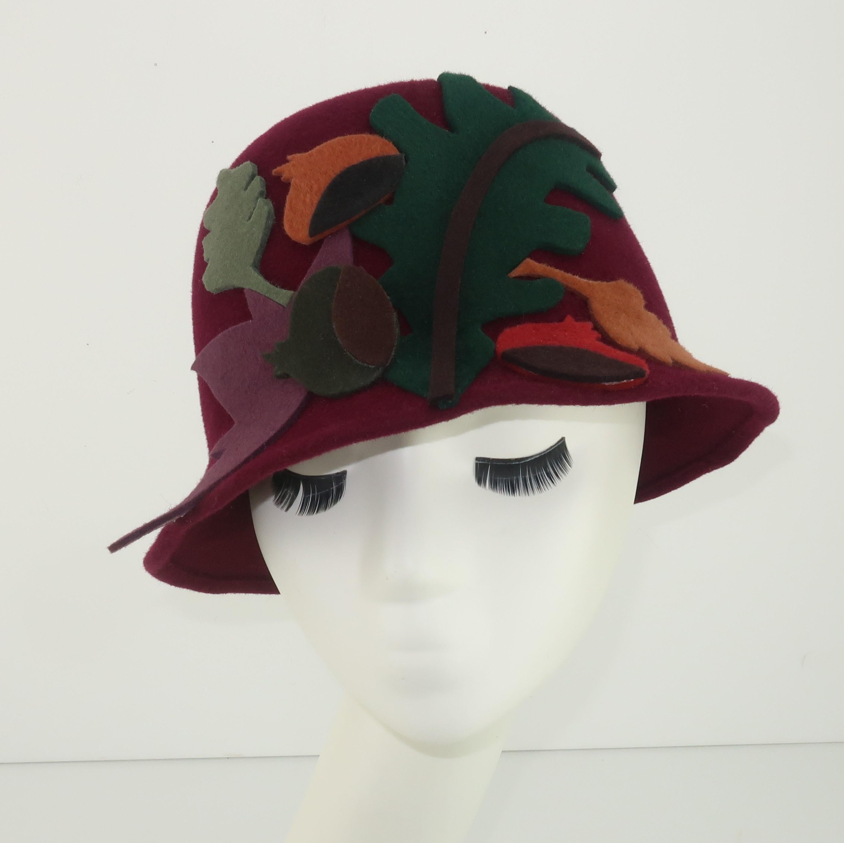 Belgian designer, Elvis Pompilio, offers a touch of autumn with this 1990's wool felt bucket hat creation.   The base of the hat is a deep burgundy red which is decorated with felt appliques in abstract shapes of leaves and acorns, all in shades of