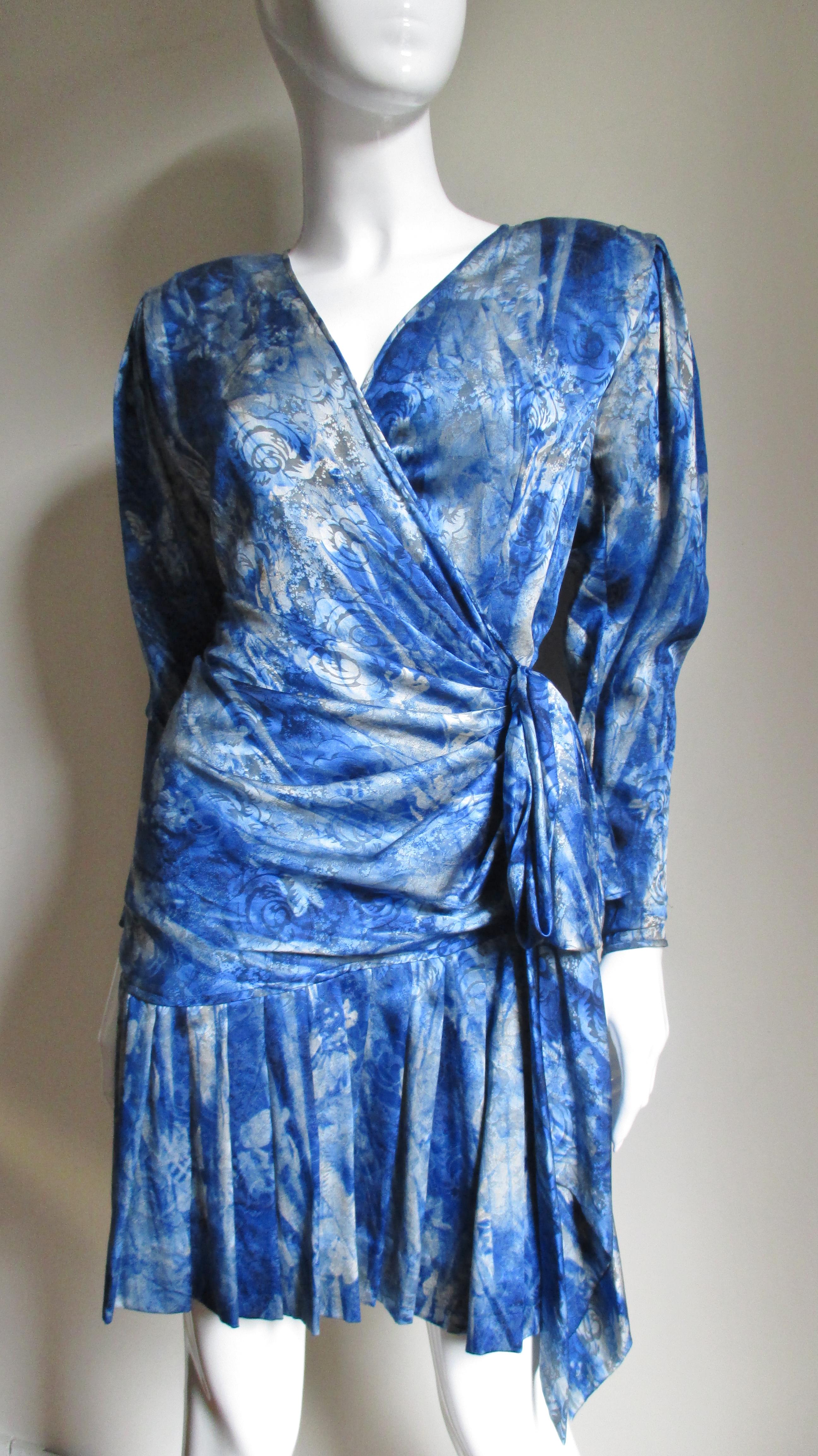 A gorgeous blue and off white elaborate abstract pattern silk damask wrap dress from Emanuel Ungaro Parallele.  It has a V neckline with a wrap semi fitted hip length bodice tying at the side waist.  The long sleeves have zipper cuff sleeves with