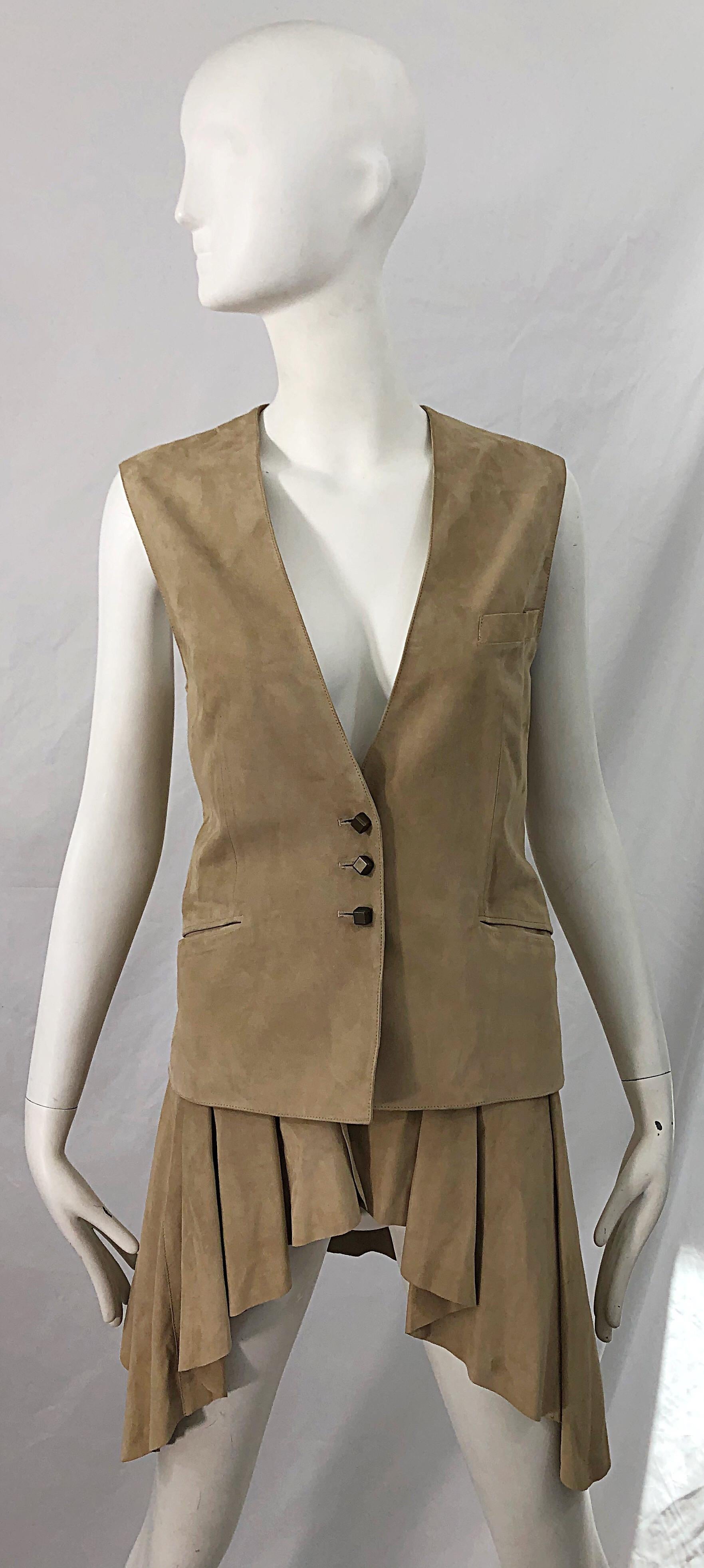 Stylish late 90s EMANUEL UNGARO tan suede leather sleeveless dip hem vest jacket ! Features the softest most luxurious suede. Three square brass buttons up the front. Pockets at each side of the waist and at left breast. Fully lined. Can easily be