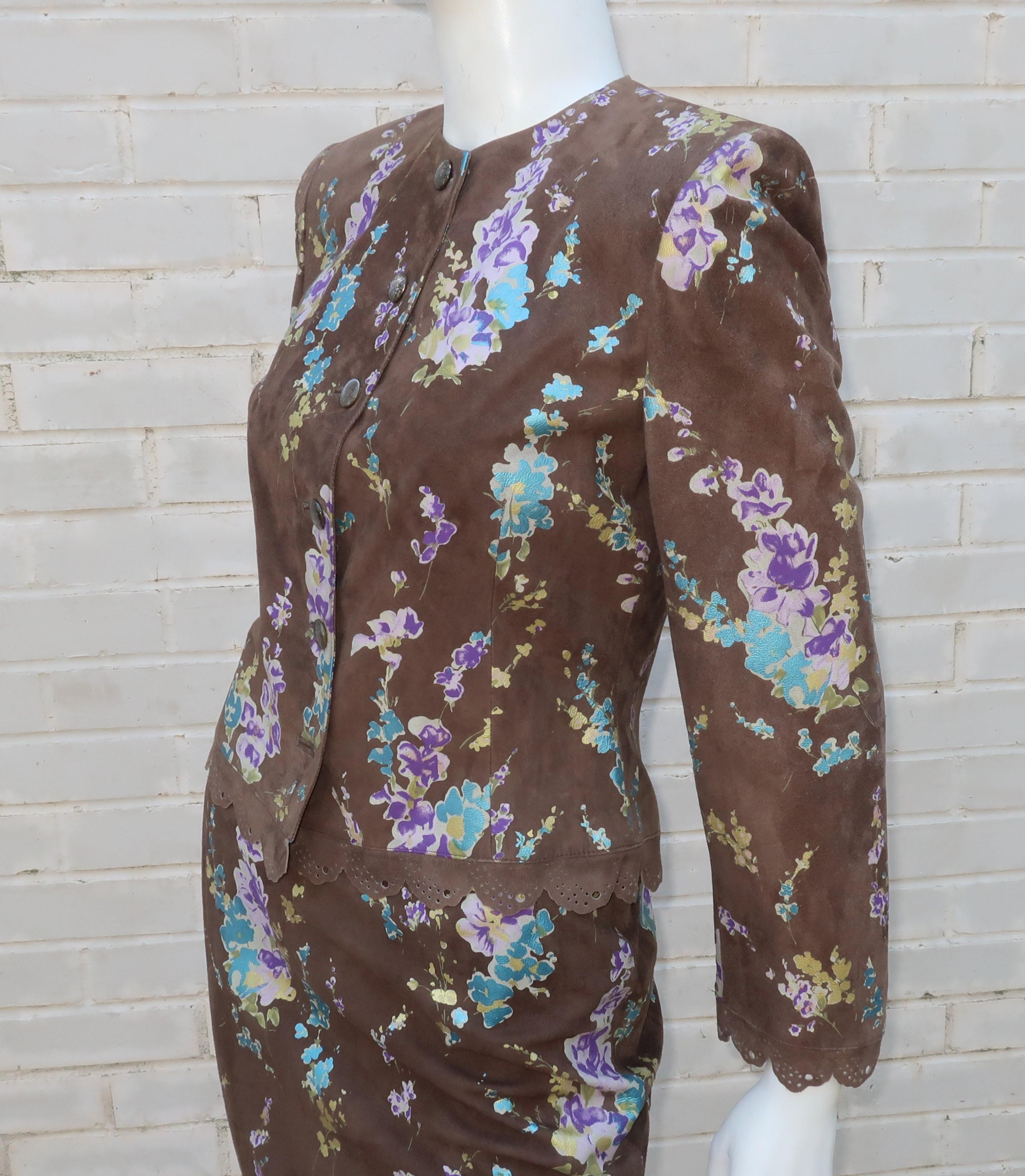 A unique Emanuel Ungaro 1980's skirt suit design in a supple brown suede with a floral transfer pattern in shades of matte gold, metallic blue and purple.  The collarless jacket buttons up the front with pierced scallop details at the cuffs and hem.