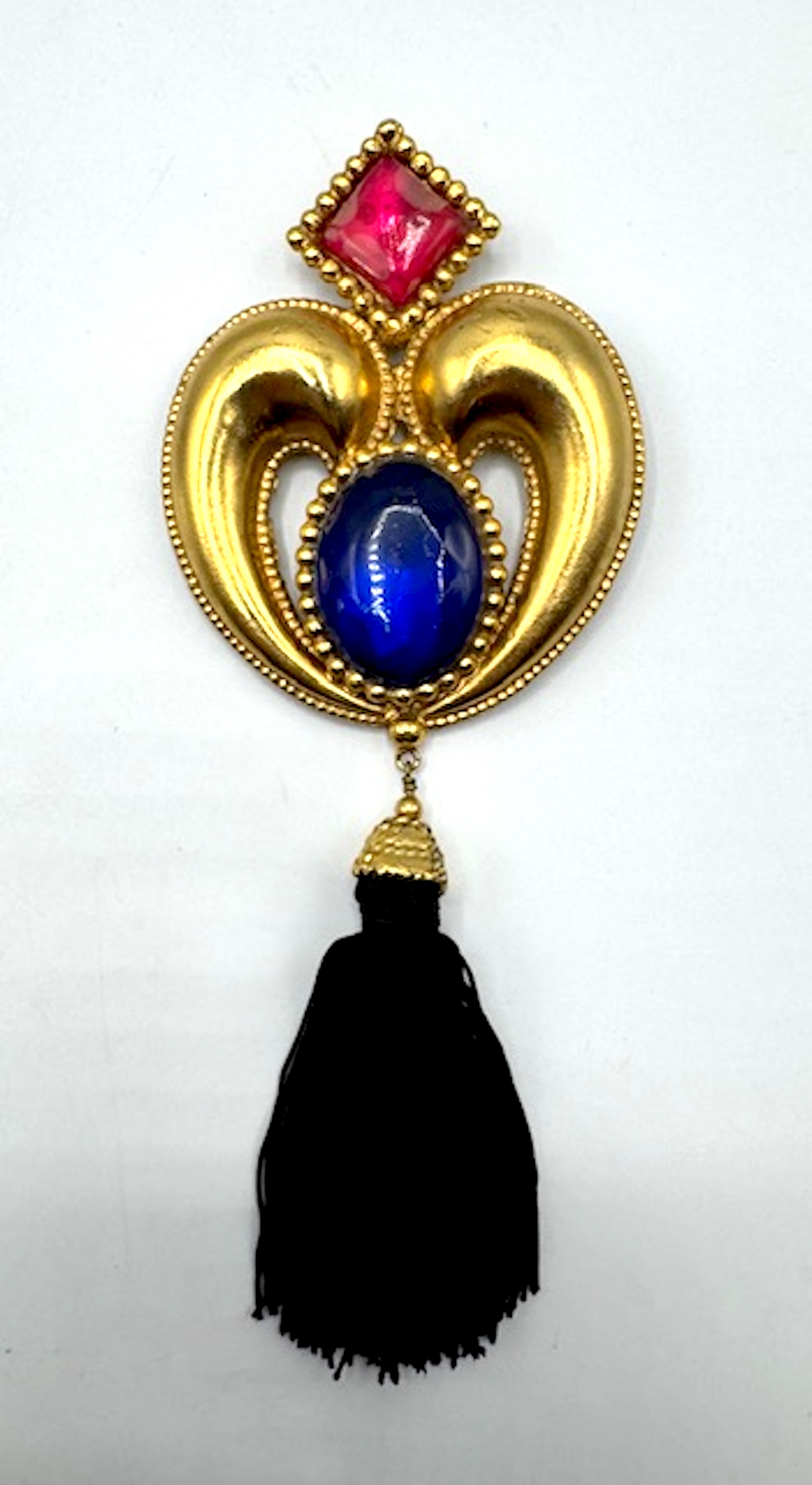 Vintage 1980s Emanuel Ungaro very large brooch featuring a heart shaped design in gold plate with tassel. It is adorned with a square red and an oval blue resin cabochon. The brooch measures 3 inches wide and 7.5 inches long. The back has an oval