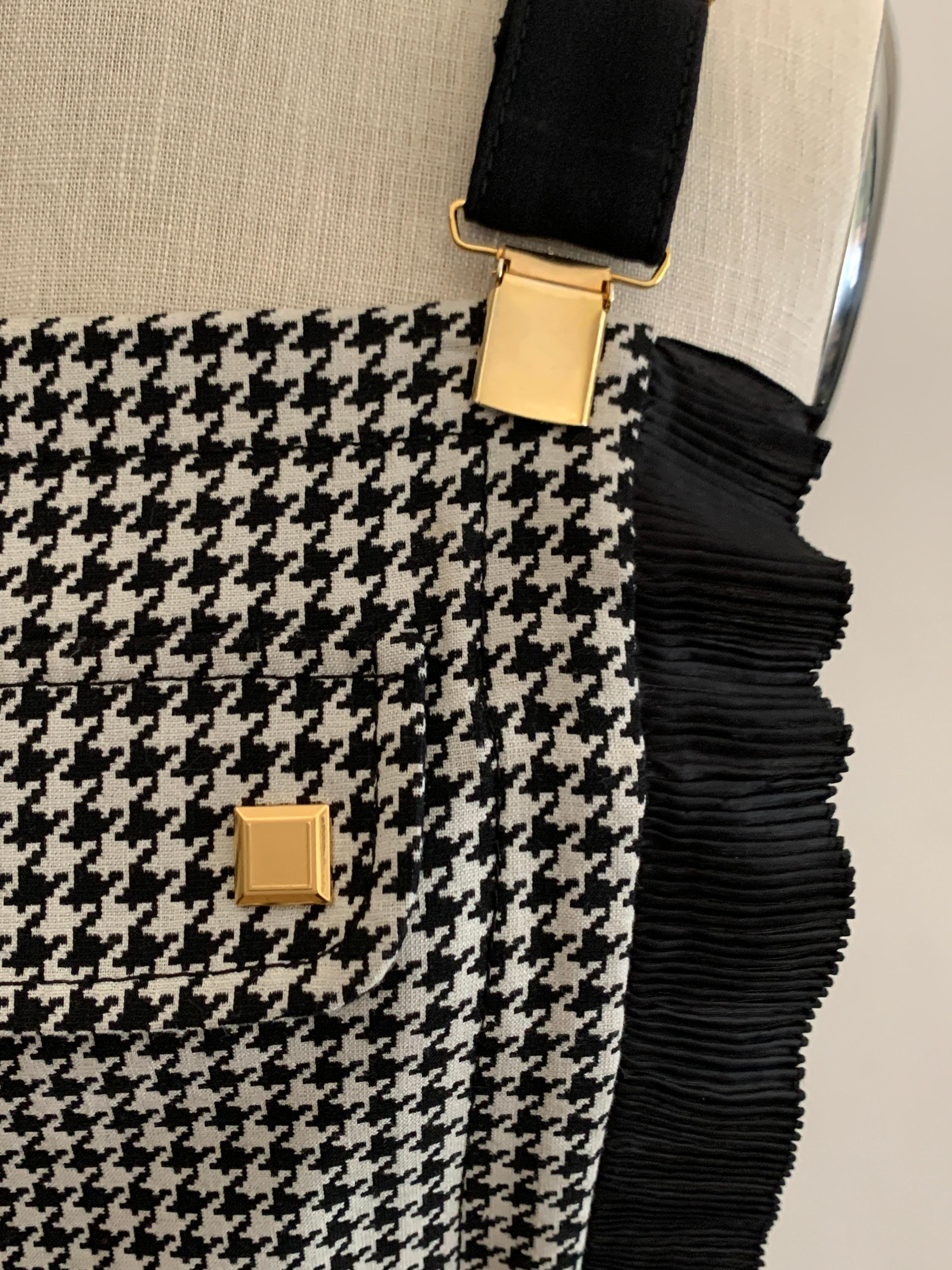 Emanuel Ungaro black and white houndstooth check resort 2014 dress with suspender style straps and pleated trim detail. Faux pocket flap at front with gold stud detail. Side zip.

Made in Italy.

55% wool, 44% rayon, 1% other.
Fully lined in 60%